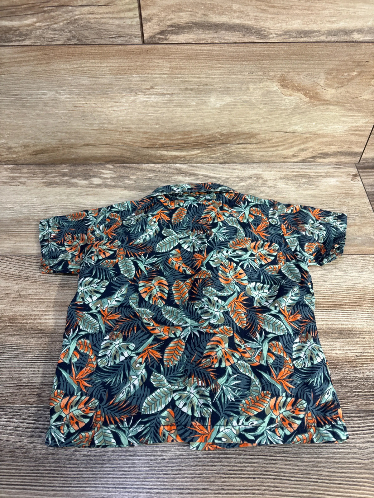 Front view of Mick Mack floral button-up shirt in green showcasing tropical print on a wood background
