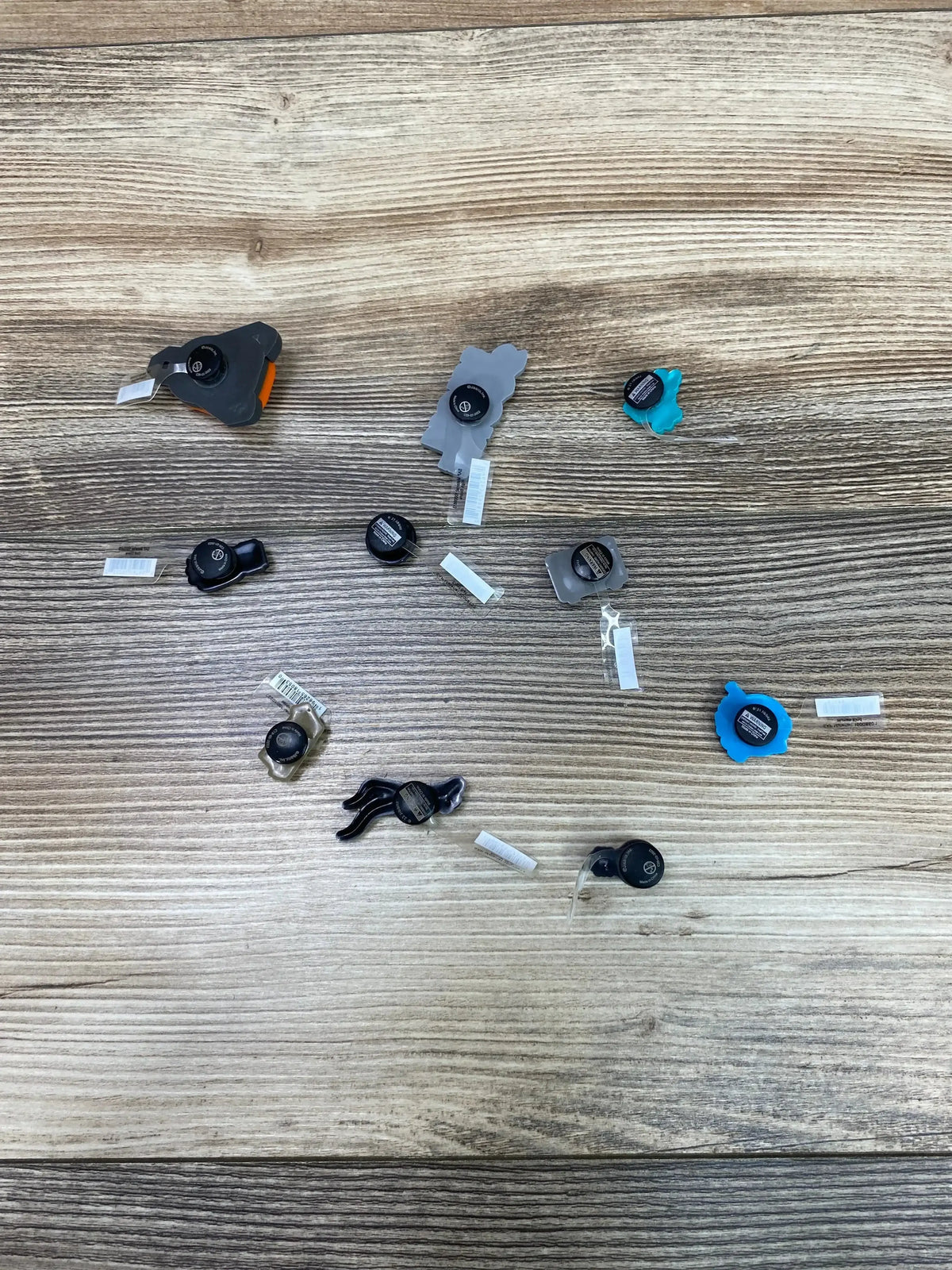 Top view of 10 Croc Jibbitz charms in assorted shapes and colors with retail tags on a wood-grain surface