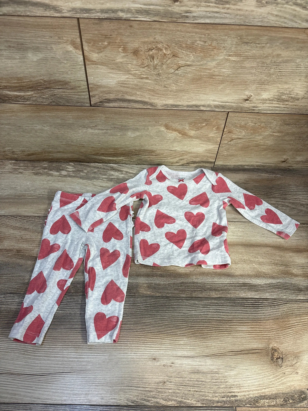 Top view of Carter’s two-piece heart print shirt and pants set showcasing gray fabric on a wood floor