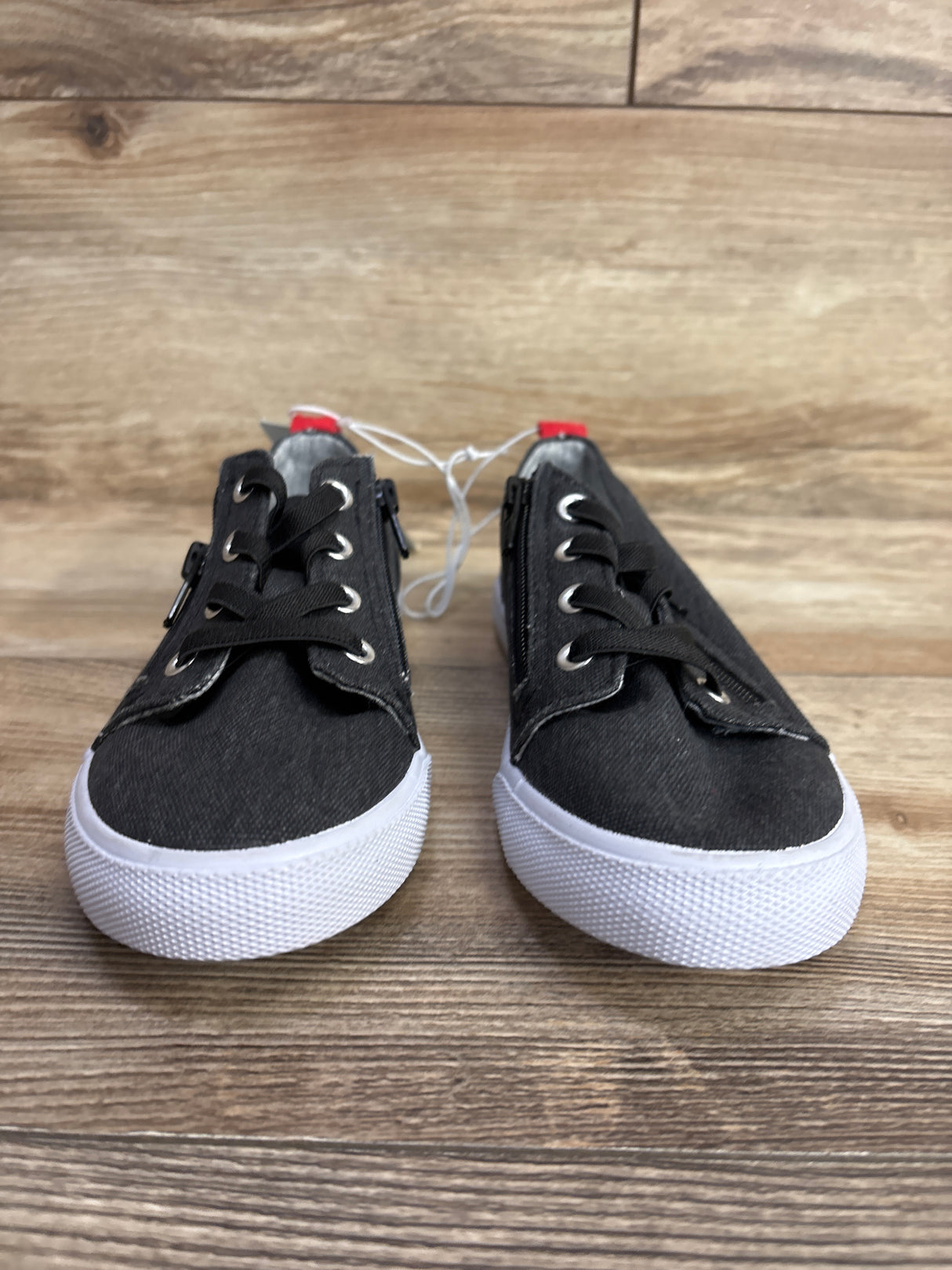 Pair of black toddler sneakers with white soles on wood background, children's shoes with laces and zippers