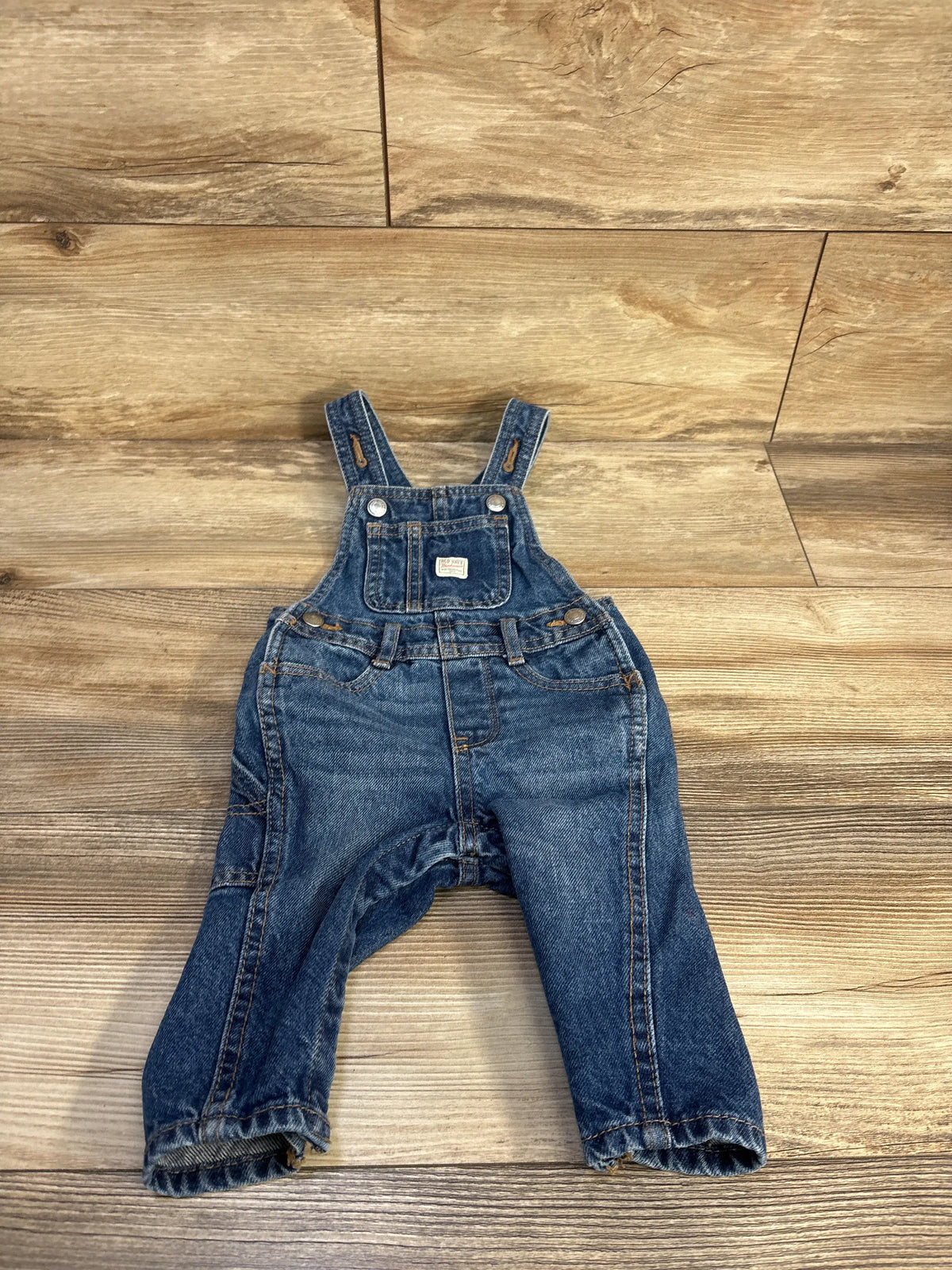 Old Navy workwear denim overalls for babies in blue, size 6-12m, on a wood floor background.