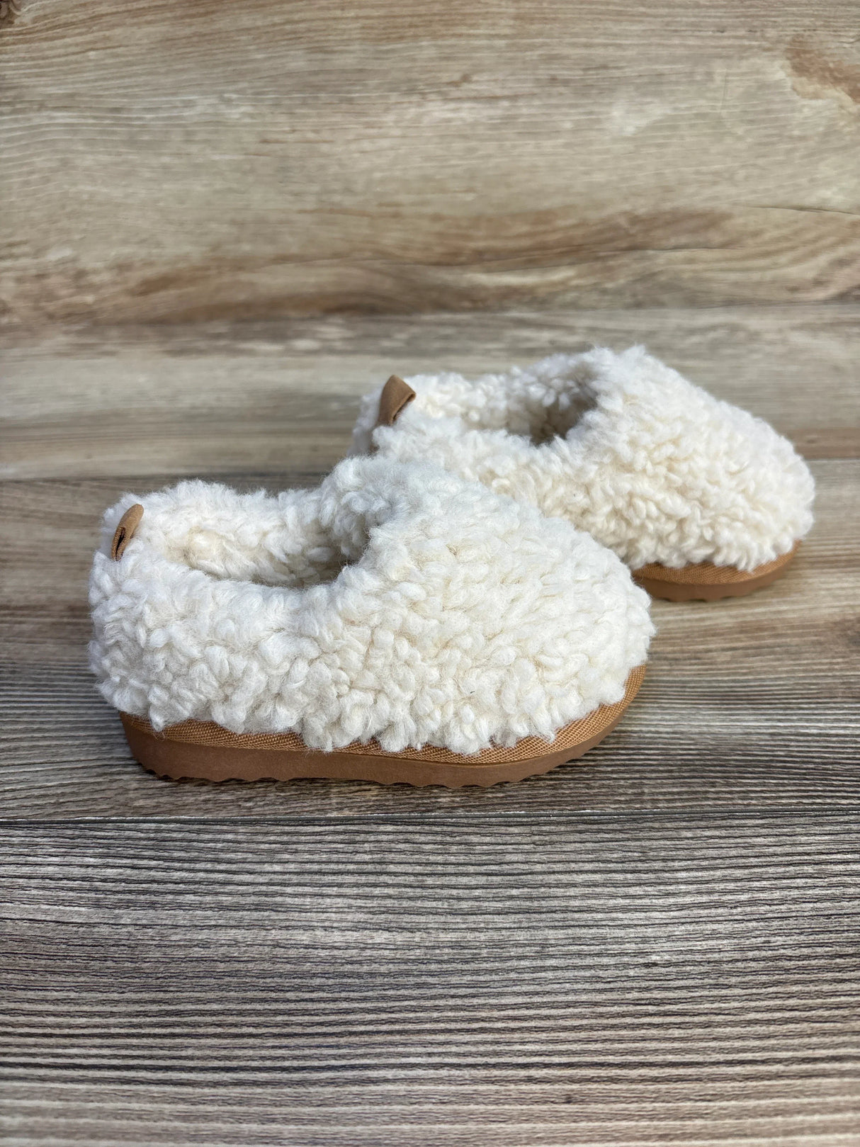 Pair of cozy cream baby booties with soft knit texture and brown soles on wood background