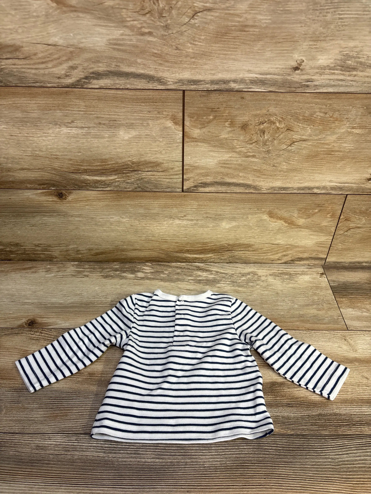 Front view of Little Me striped long sleeve shirt showcasing white fabric with navy stripes and relaxed fit on wooden background
