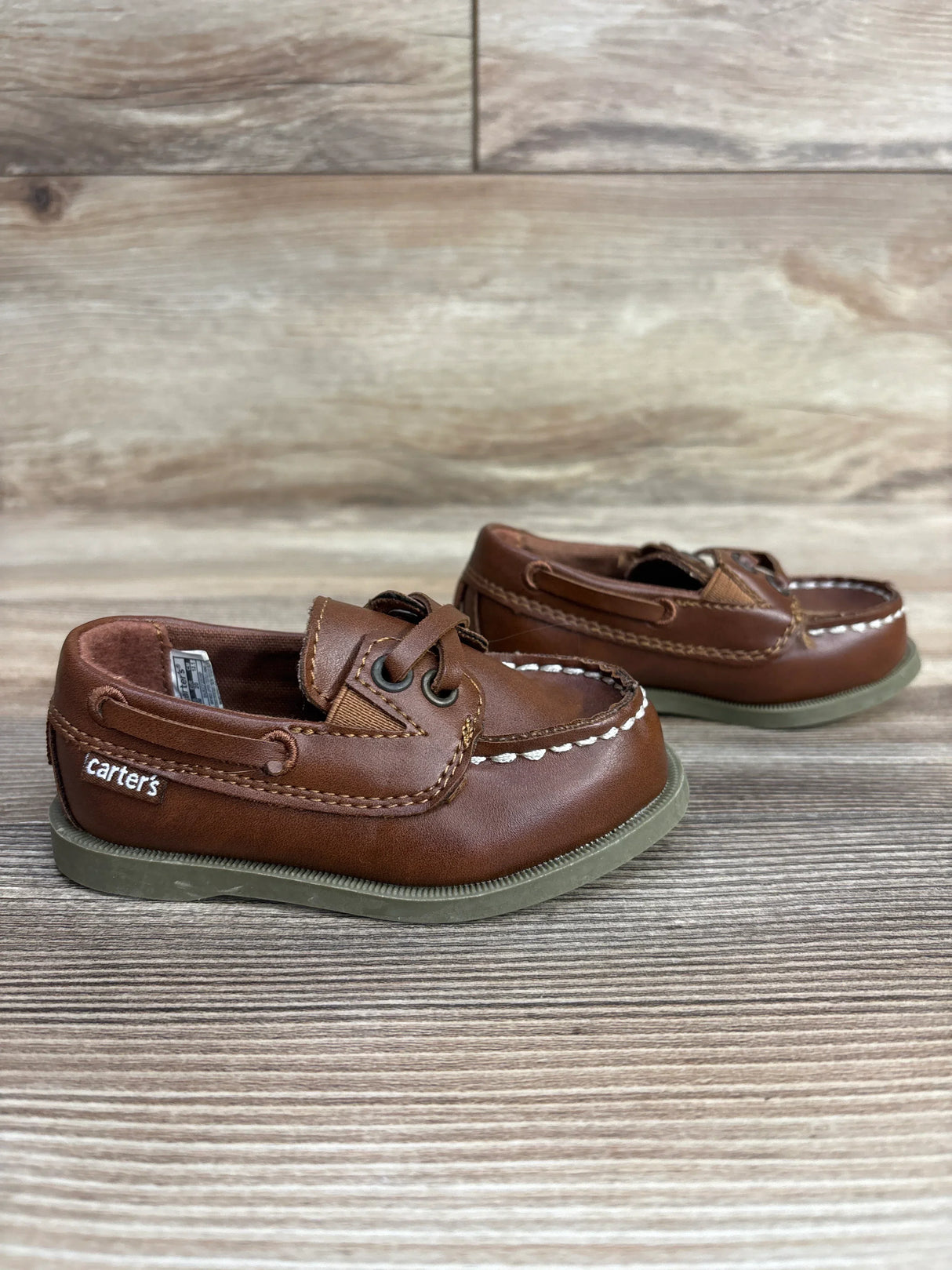 Brown Carter's toddler leather boat shoes with white stitching and gray soles on wooden surface