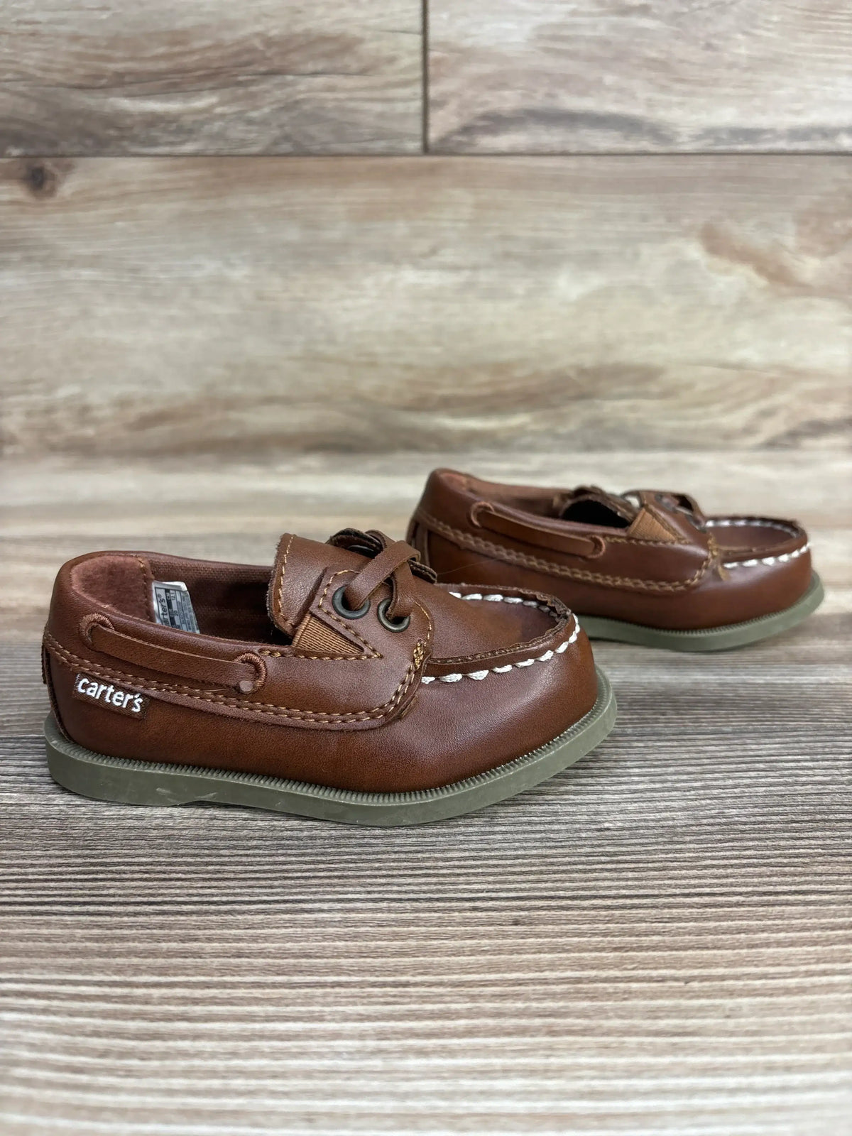 Brown Carter's toddler leather boat shoes with white stitching and gray soles on wooden surface