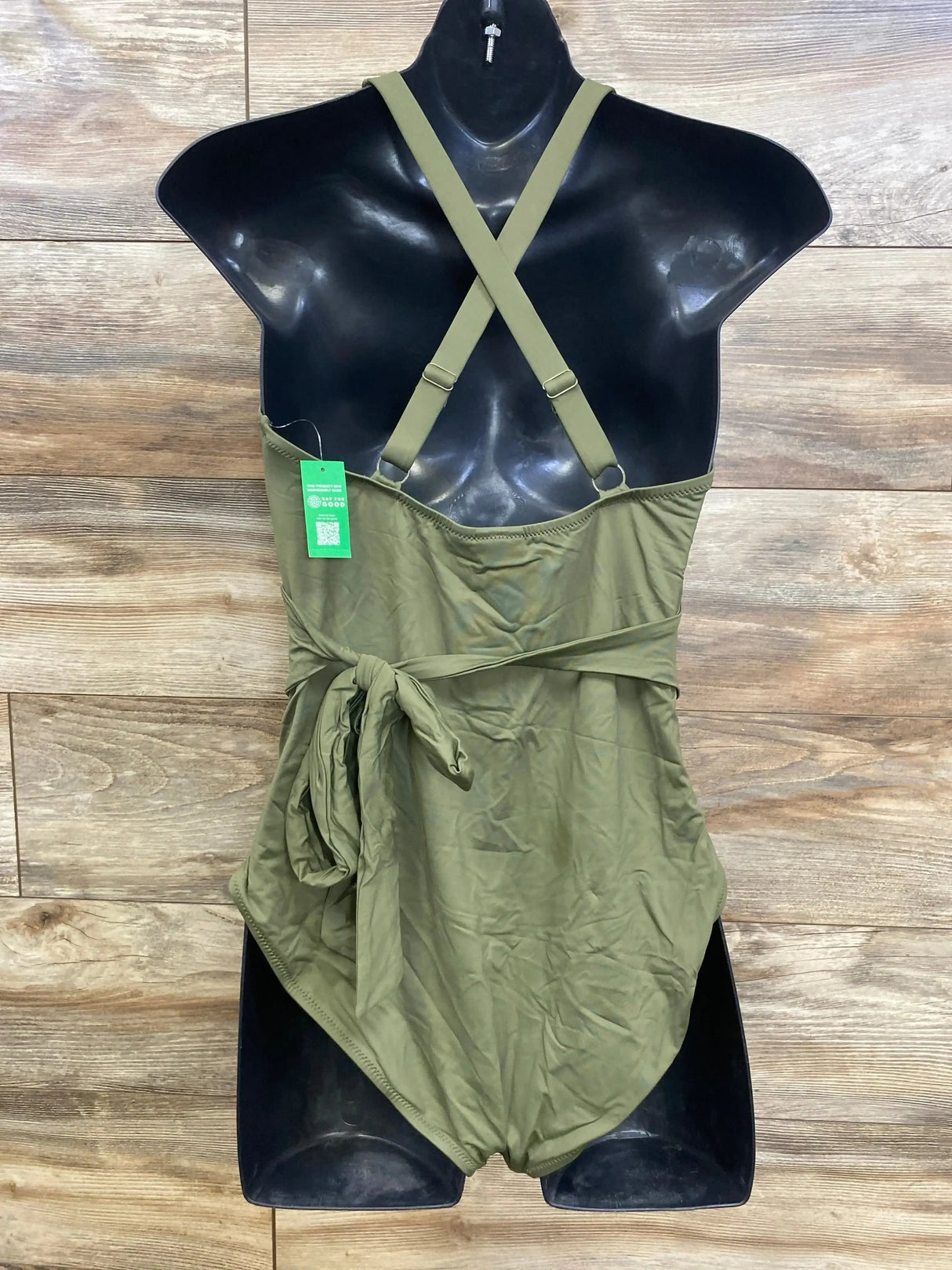 Front view of green maternity 1-piece wrap swimsuit with crisscross straps and waist tie on black mannequin against wood wall