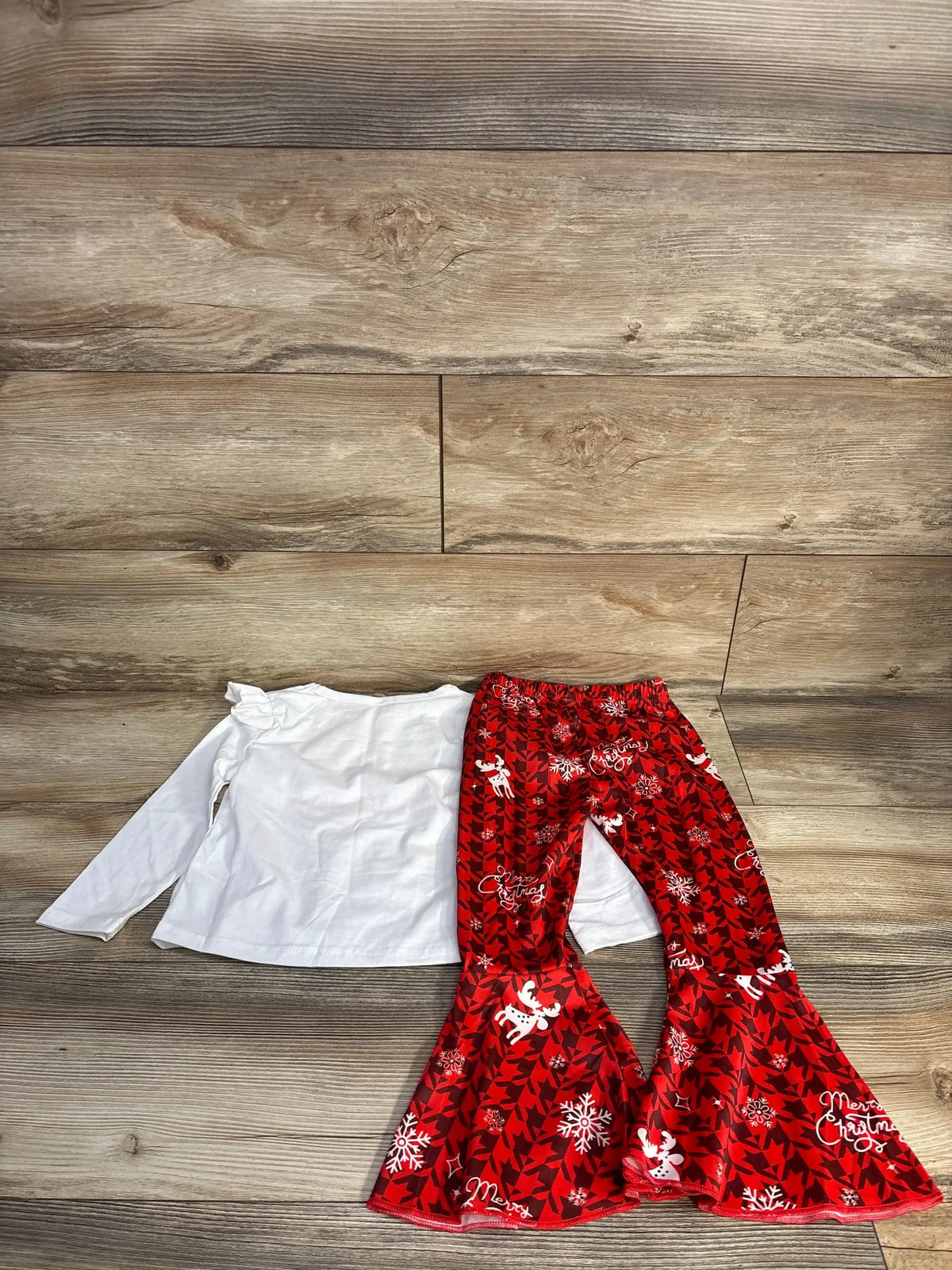White long-sleeve baby shirt with ruffled shoulder and red Christmas-themed bell-bottom pants on wood background