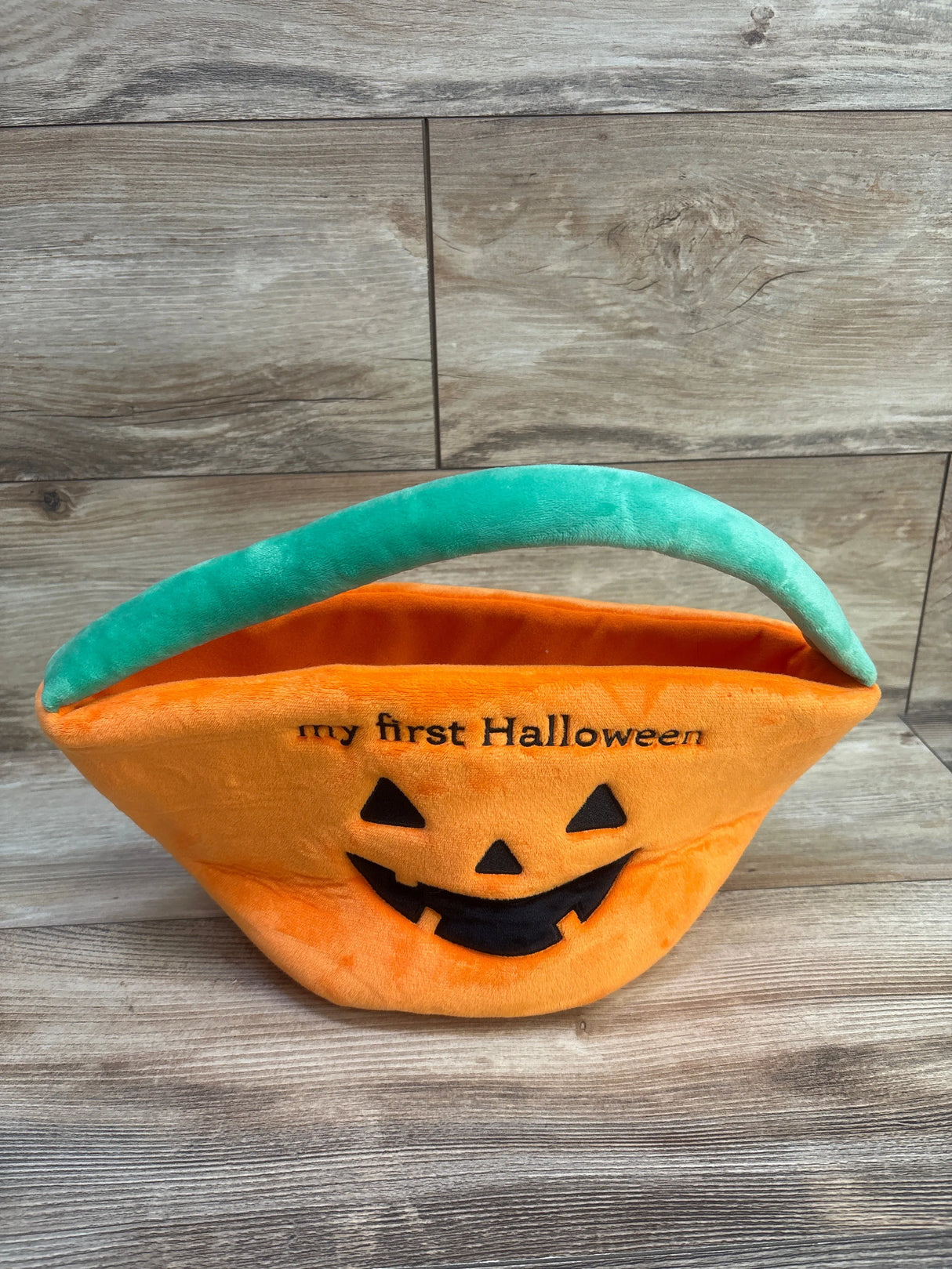 Front view of orange pumpkin treat bag with embroidered my first Halloween text, jack-o’-lantern face and green handle