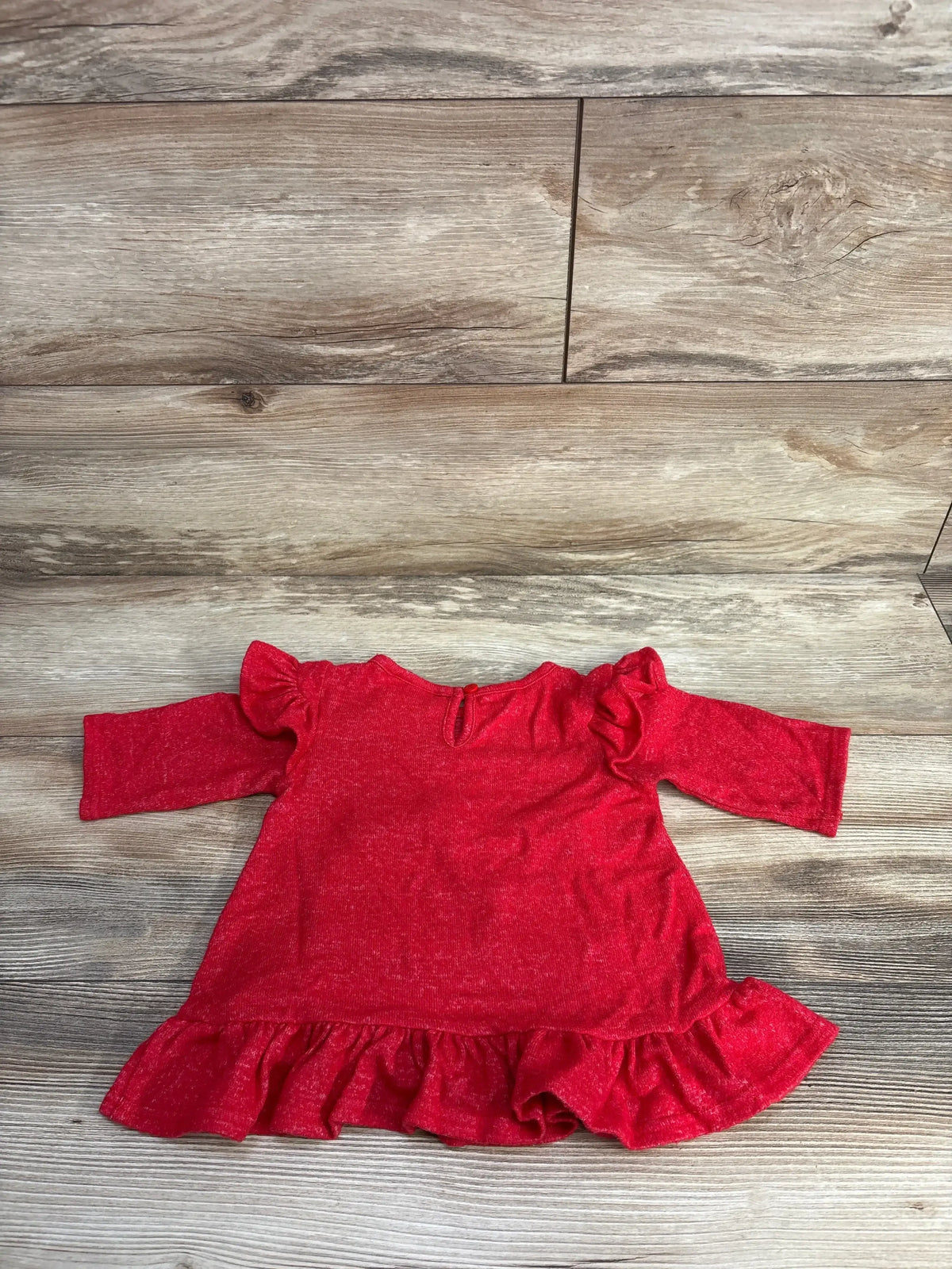 Red baby dress with ruffled sleeves and hem, laid on wooden floor