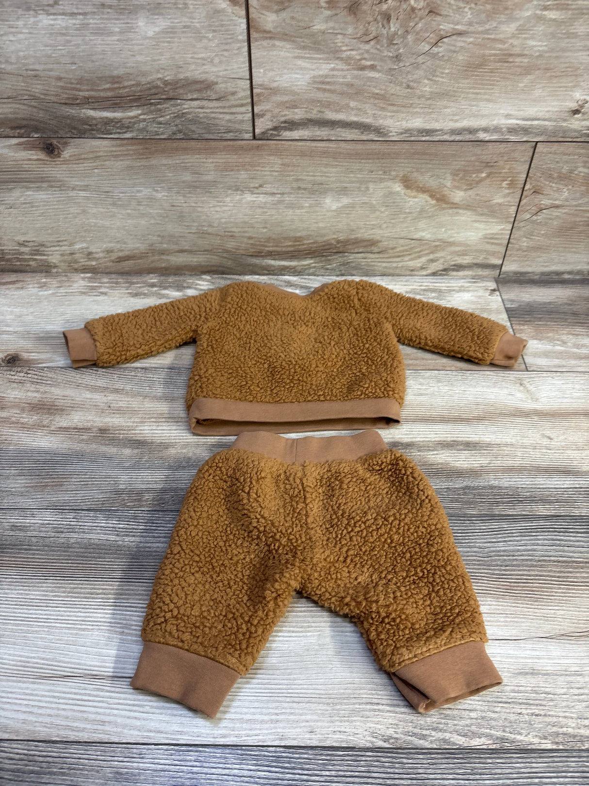 Flat lay of newborn brown faux-fur pullover and joggers set showcasing soft teddy fleece on wood background