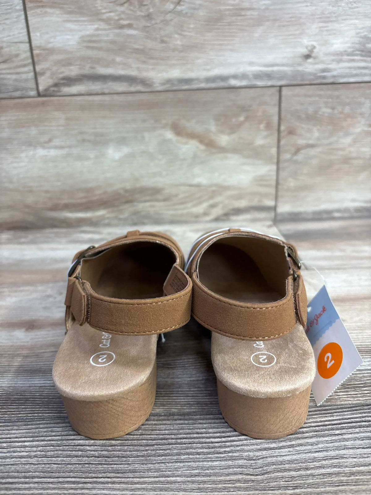 Pair of toddler size 2 brown sandals with adjustable straps on wooden floor background