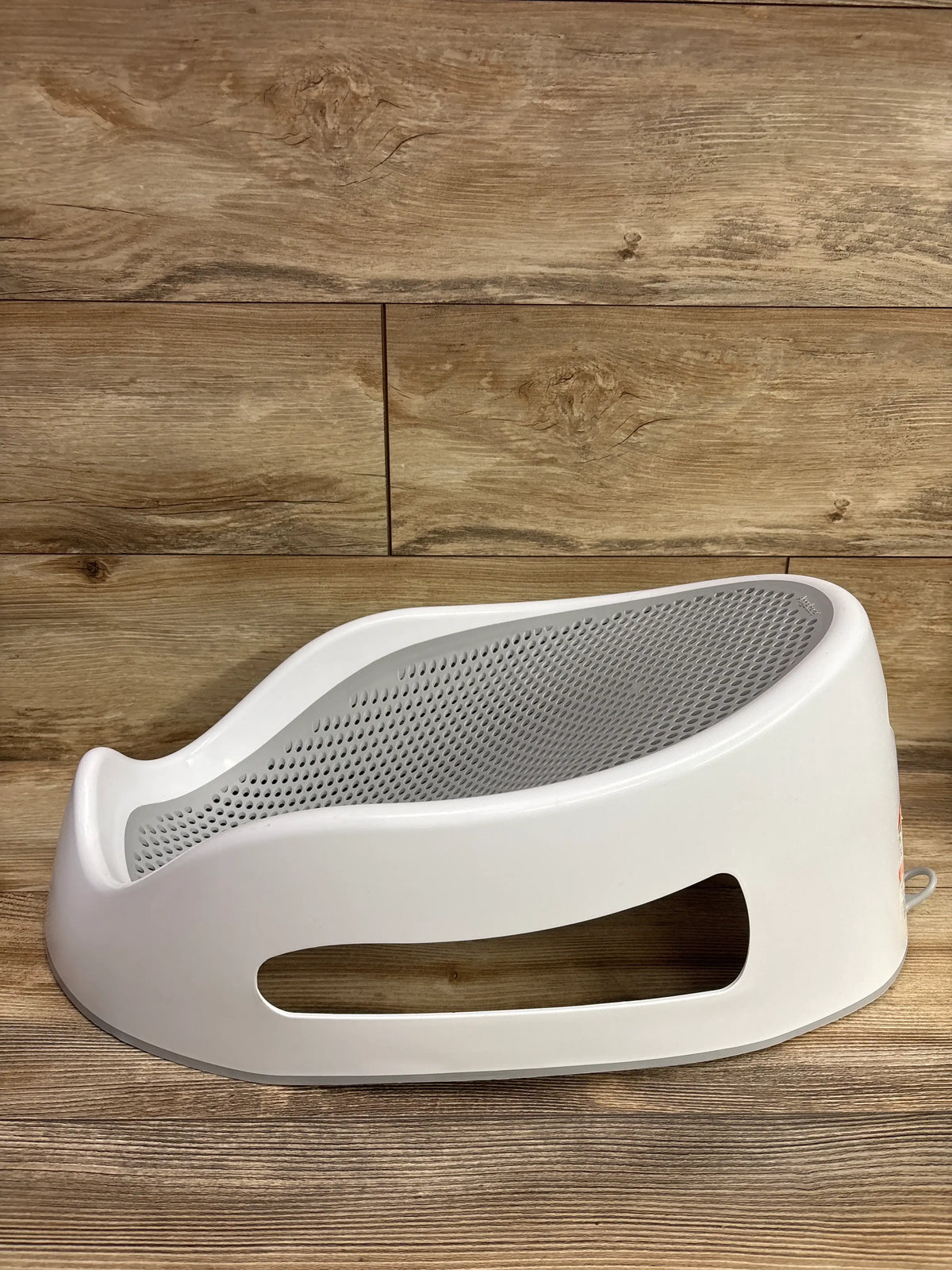 Angled view of Angelcare Bath Support in grey showcasing perforated mesh seat and side opening on wood flooring