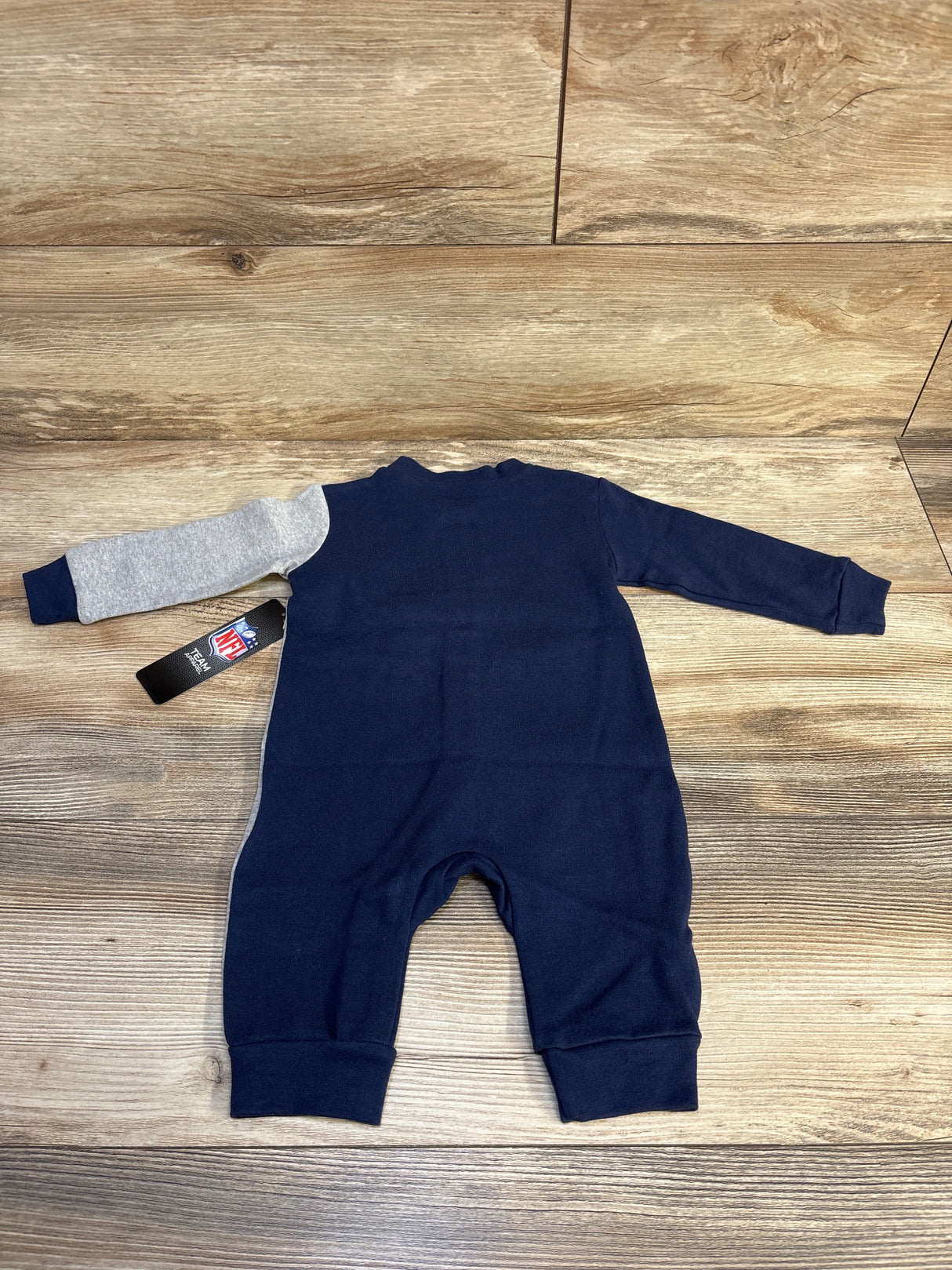 Navy blue and grey long-sleeve infant romper laid flat on wooden surface with NFL tag attached