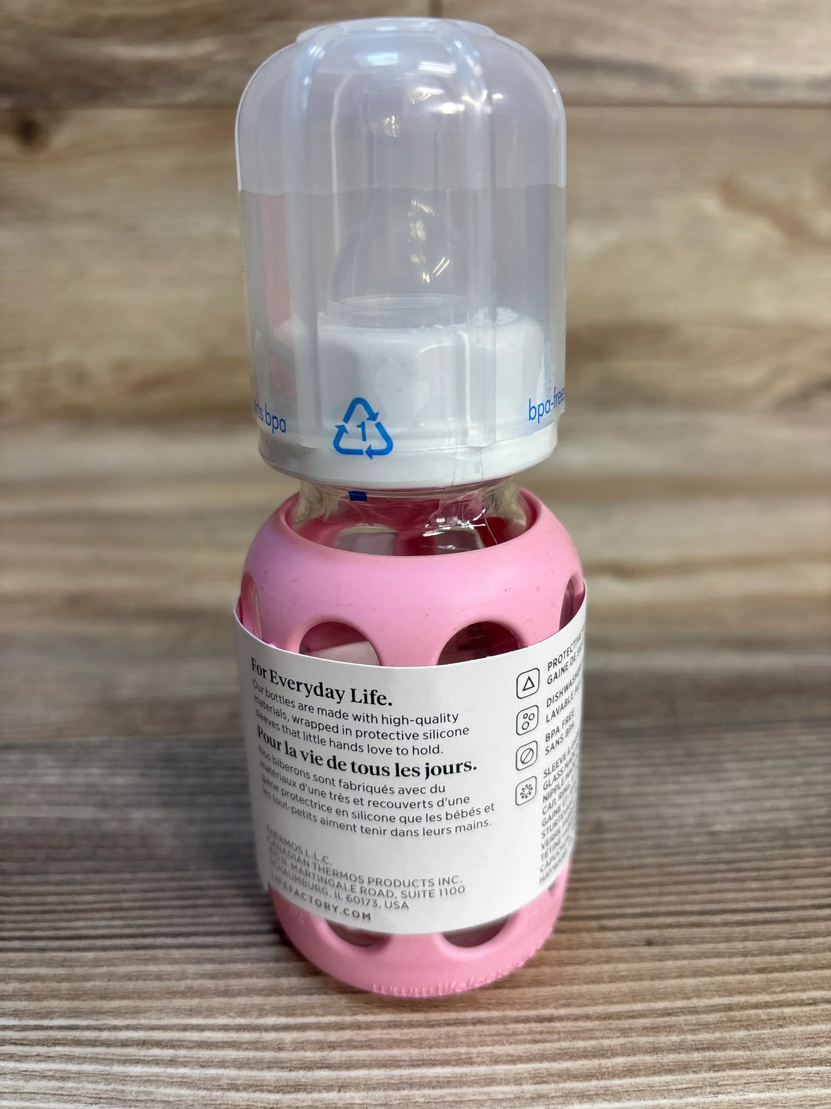 Glass baby bottle with pink silicone sleeve and clear cap on wood background