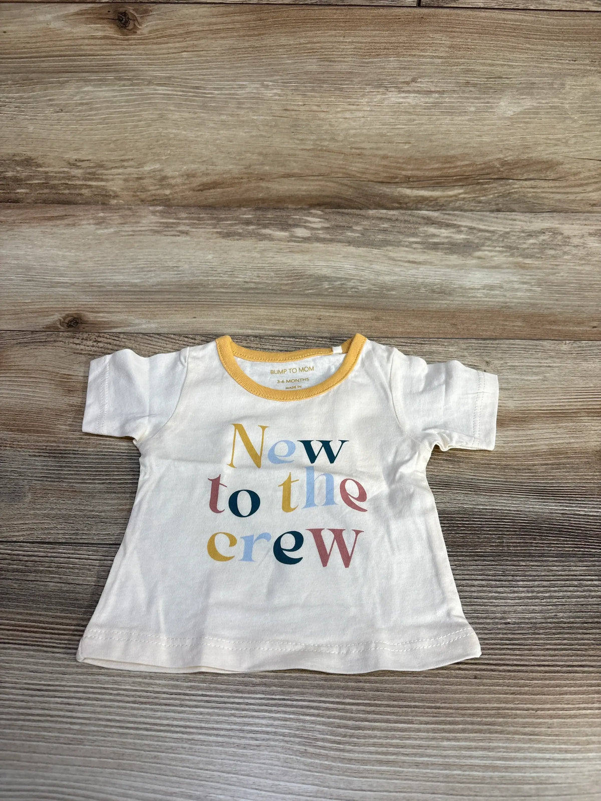 Baby t-shirt with 'New to the crew' text in pastel colors on wood background