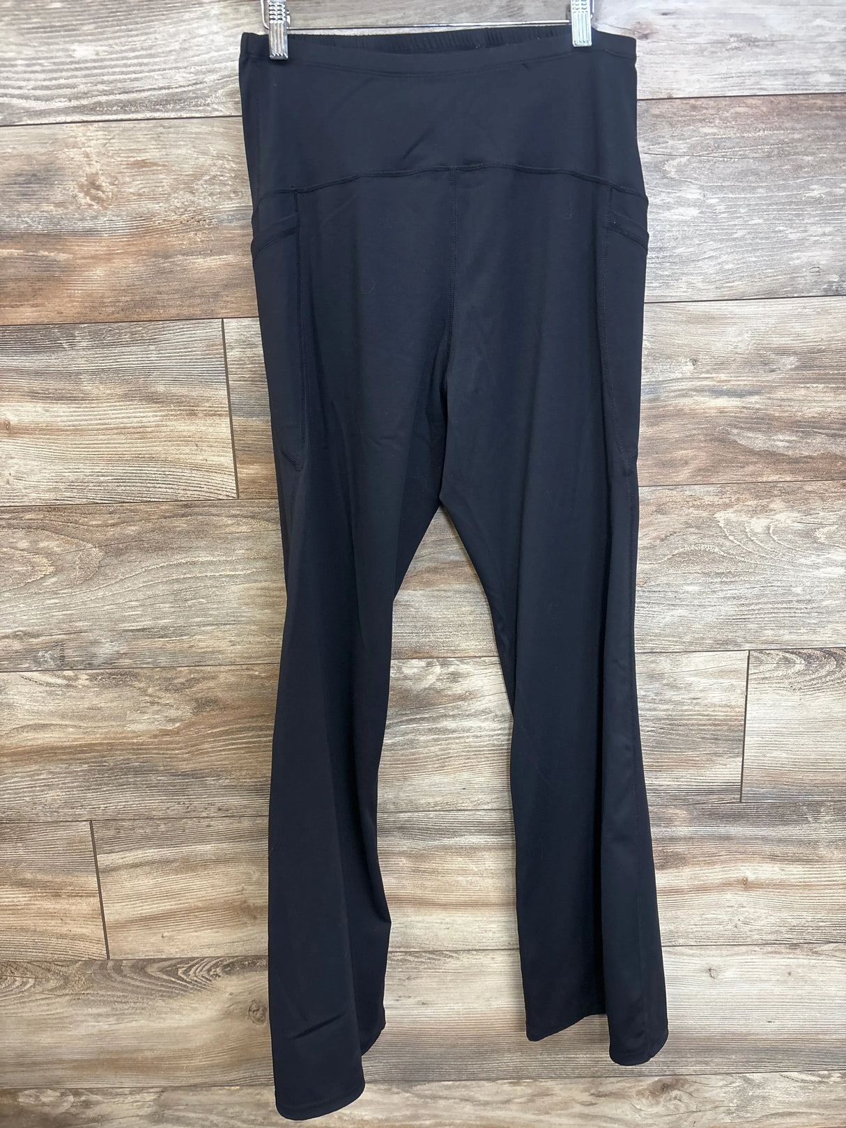 Front view of black maternity flared yoga pants showing high-rise over-belly band and flared legs against wood background