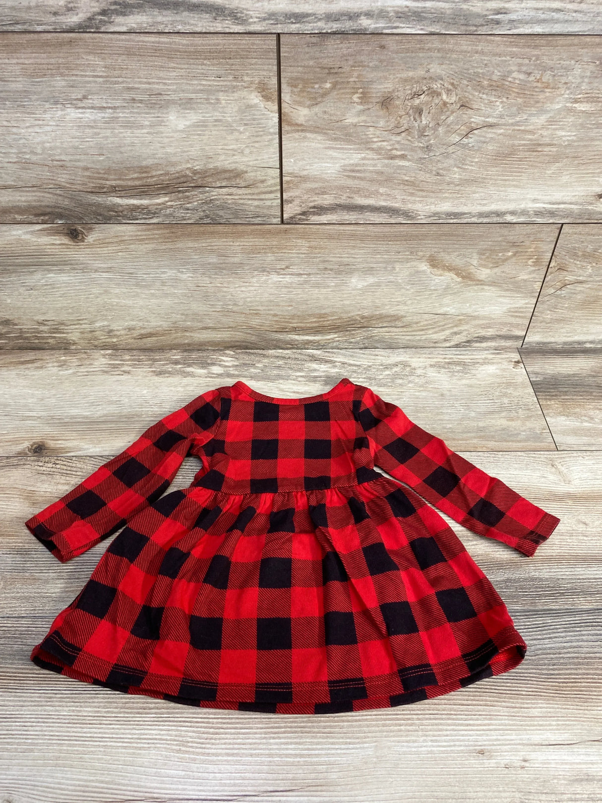 Children's red and black buffalo plaid long-sleeve dress laid flat on wood floor