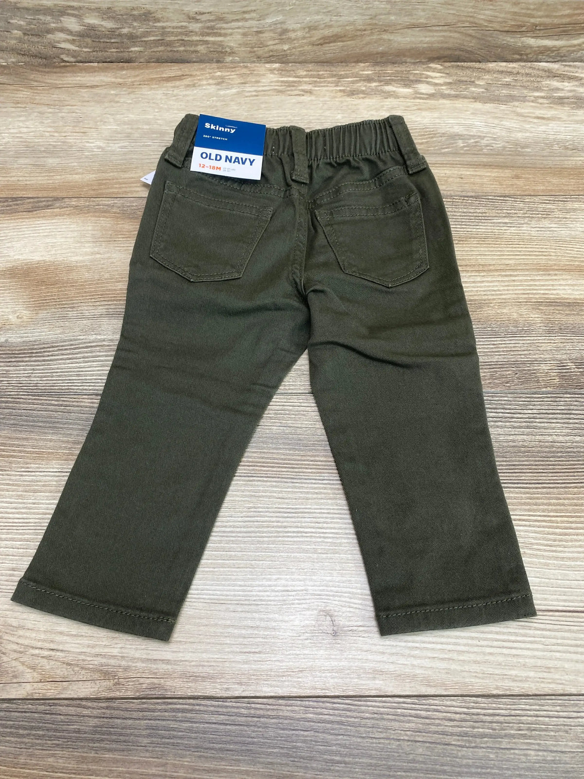 Back view of Old Navy olive toddler skinny jeans, size 12-18M, showing elastic waist and back patch pockets on wood background