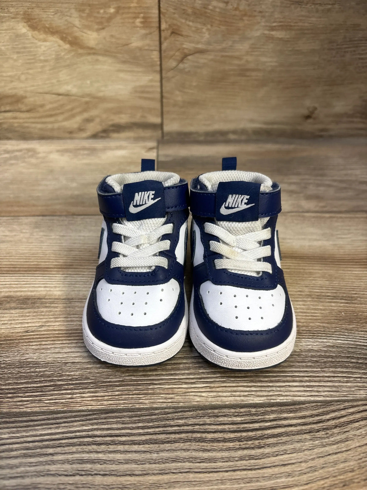 Front view of Nike Court Borough Mid 2 TD sneakers, white and signal blue high tops with Nike logos on a wood floor