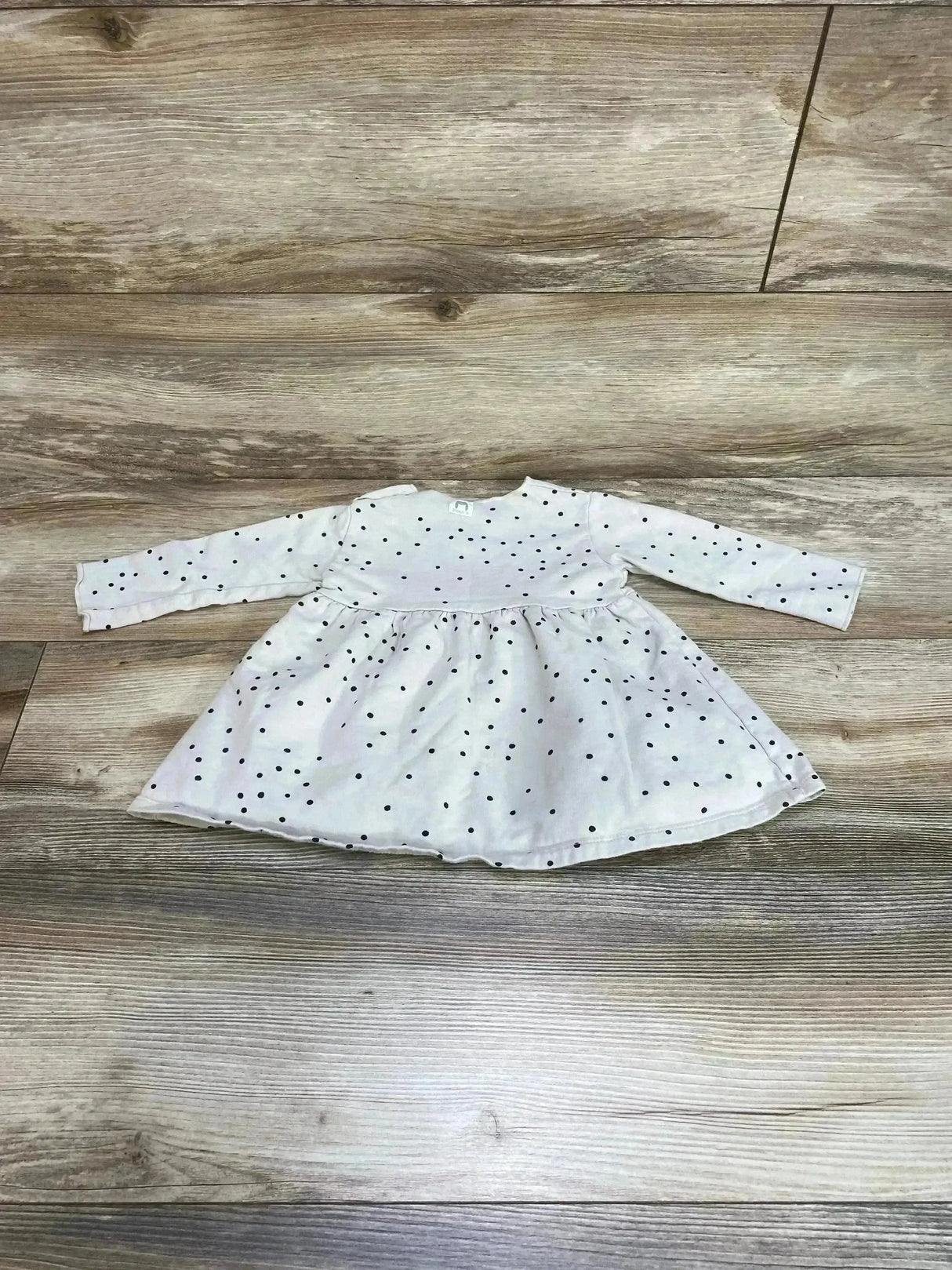 Front flat lay of 6-12M beige long-sleeve baby dress with black polka dots, gathered skirt and round neckline on wood floor