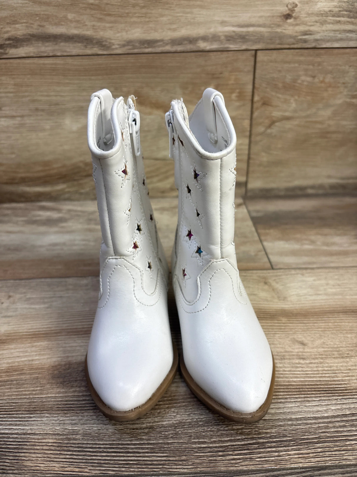 Front view of Tucker and Tate white cowgirl boots size 7C showing star cutouts with multicolor lining on wood floor