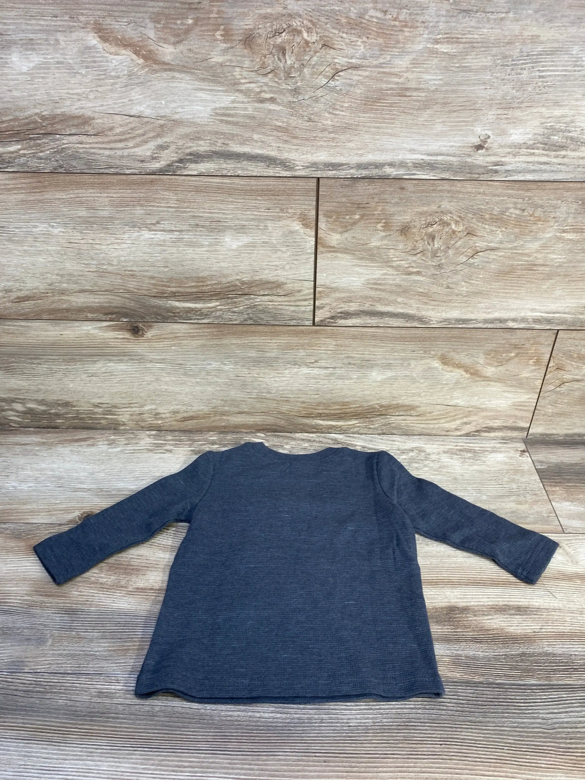Back view of Jumping Beans blue long-sleeve shirt for 12 months showing ribbed texture and crew neckline on wood plank background