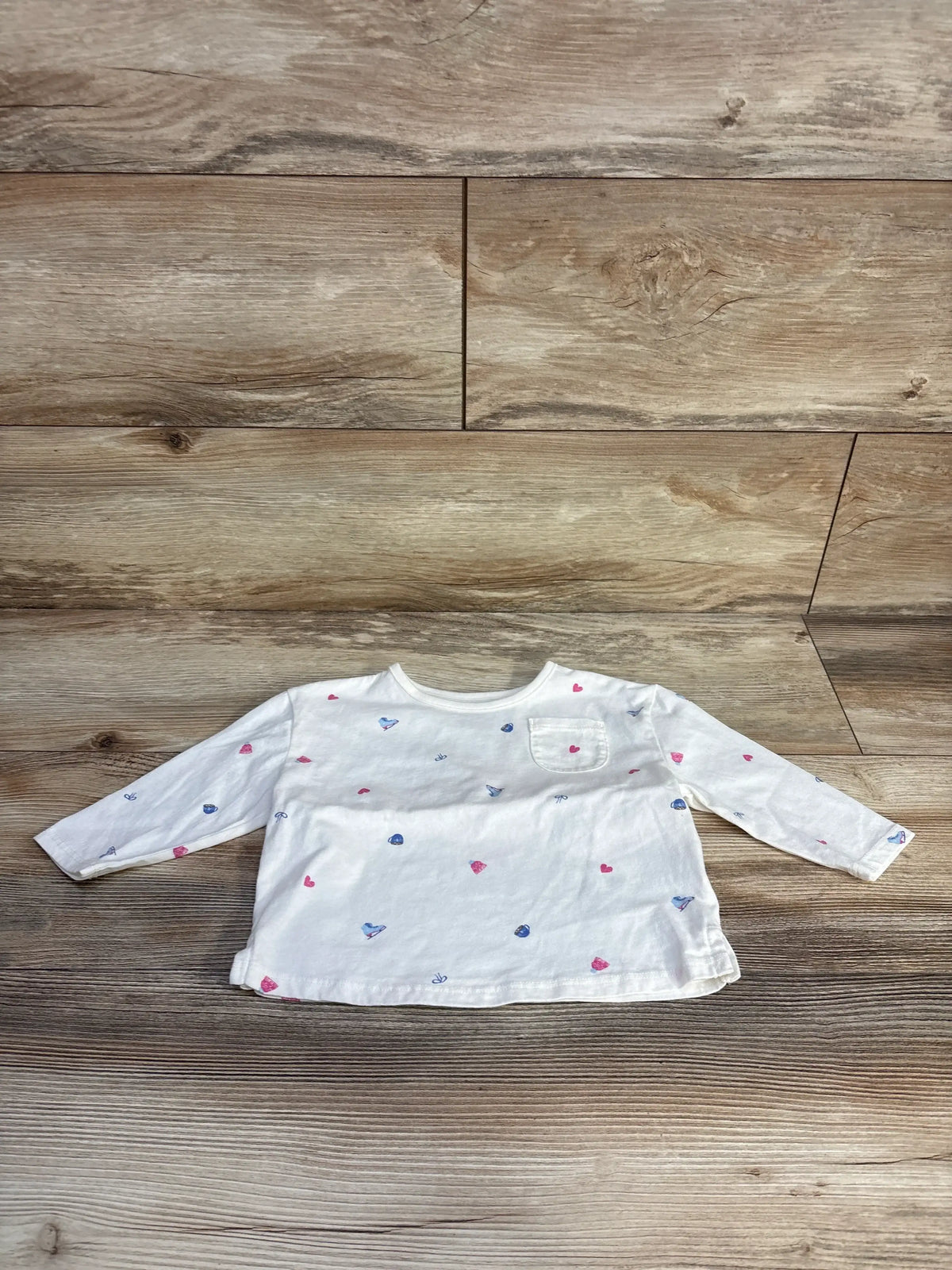 Front view of Carter’s white pocket shirt, size 18 months, showcasing long sleeves and a chest pocket on wood flooring