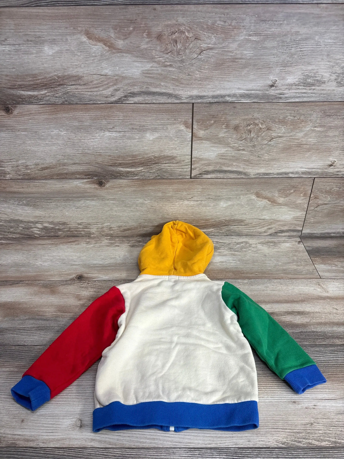 Colorblock kids hoodie with yellow hood, red and green sleeves, blue cuffs, laid on wood floor