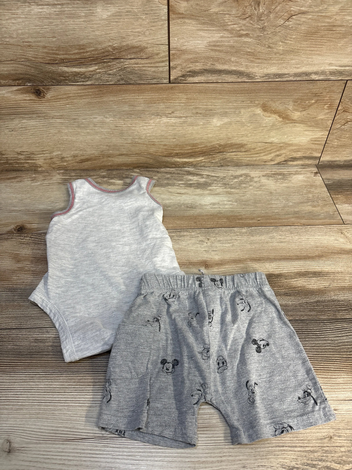 Gray sleeveless baby bodysuit with matching cartoon print shorts on wood floor