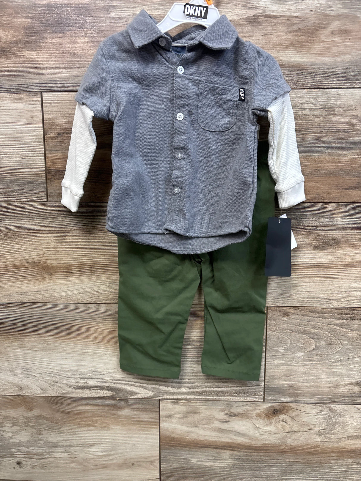 Front view of DKNY 2-piece baby set showcasing grey layered-sleeve button-up shirt and green pants on wood background