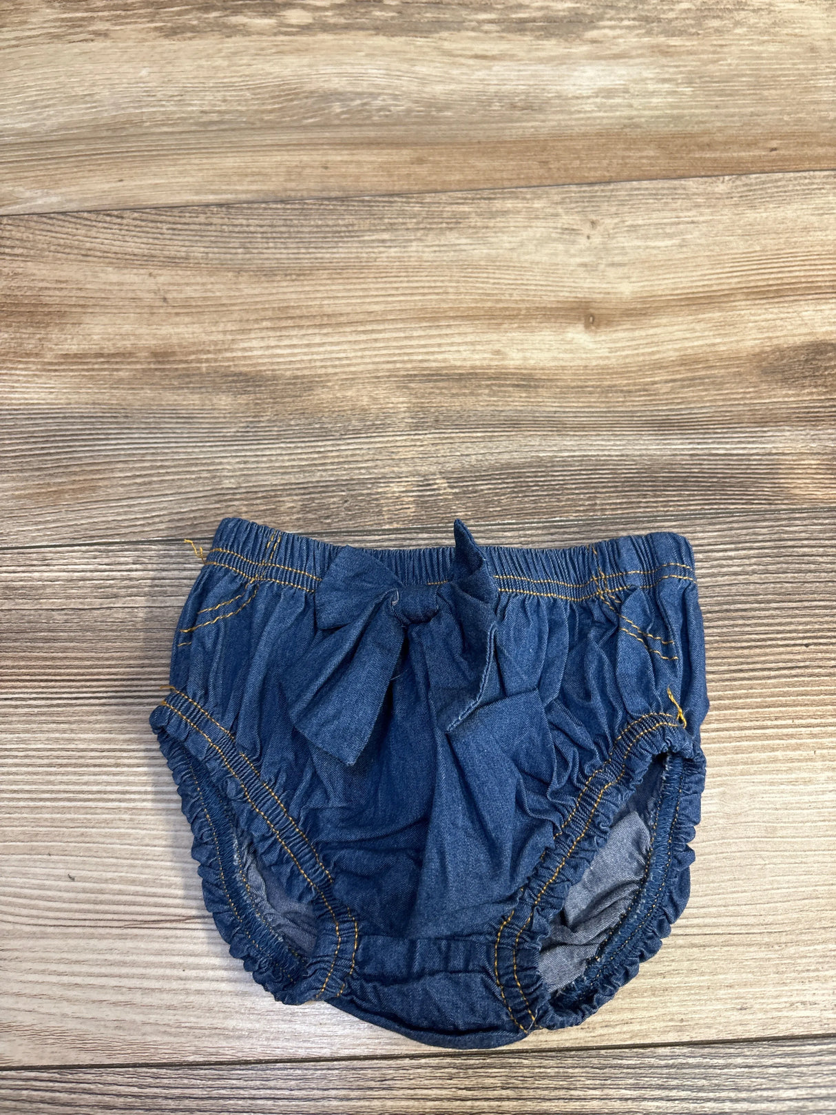 Top view of chambray blue bow bloomers with front bow, ruched details and elastic leg openings on wood background
