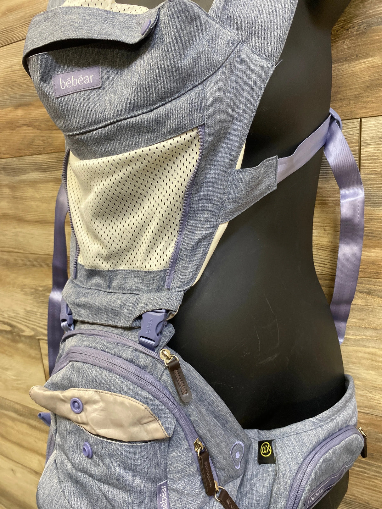 Side view of Bebear 2-in-1 hip-seat baby carrier showing mesh panel, zip pocket, and lavender straps on wood background