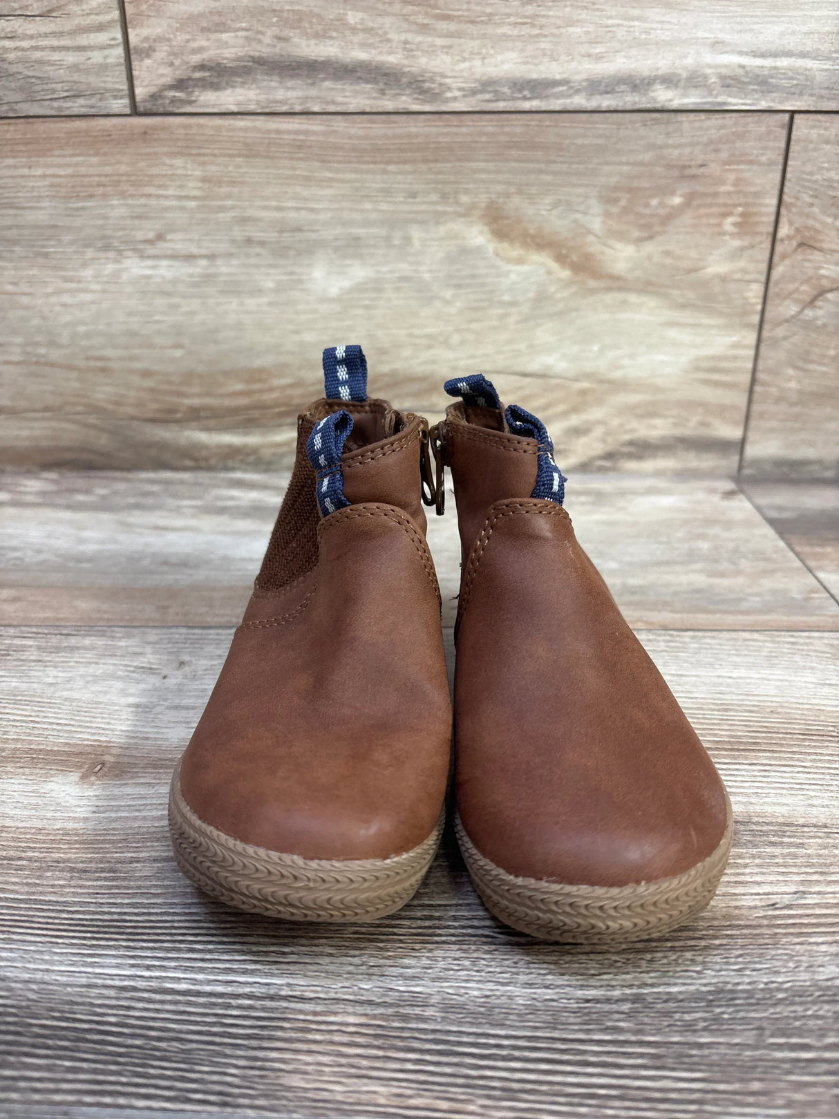 Front view of Cat & Jack Esteban Zipper Boots in brown showcasing blue pull tabs and side zippers on a wood-patterned floor