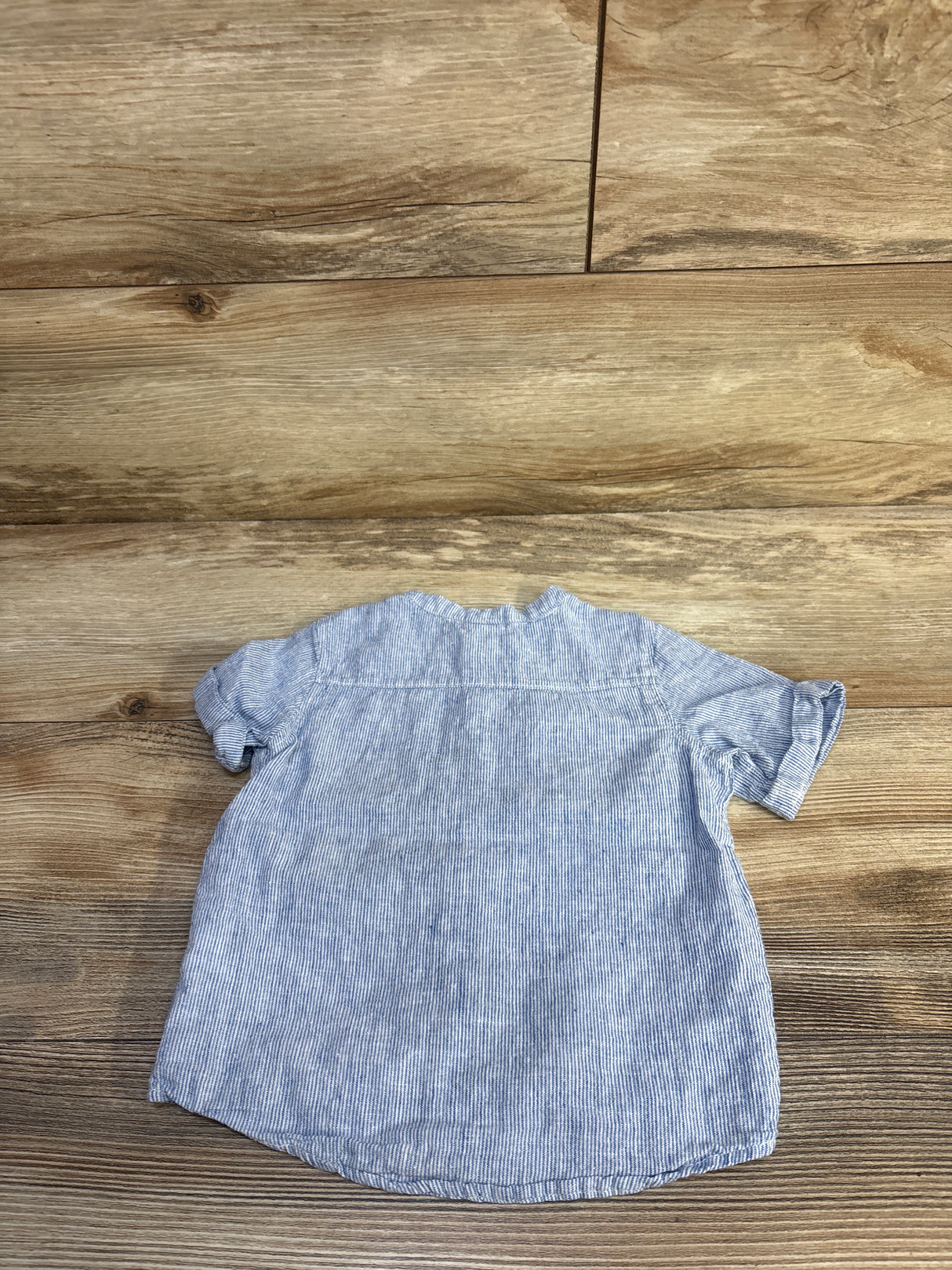 Back view of H&M baby button-up shirt size 12M showing thin blue-and-white stripes and rolled short sleeves on wood floor