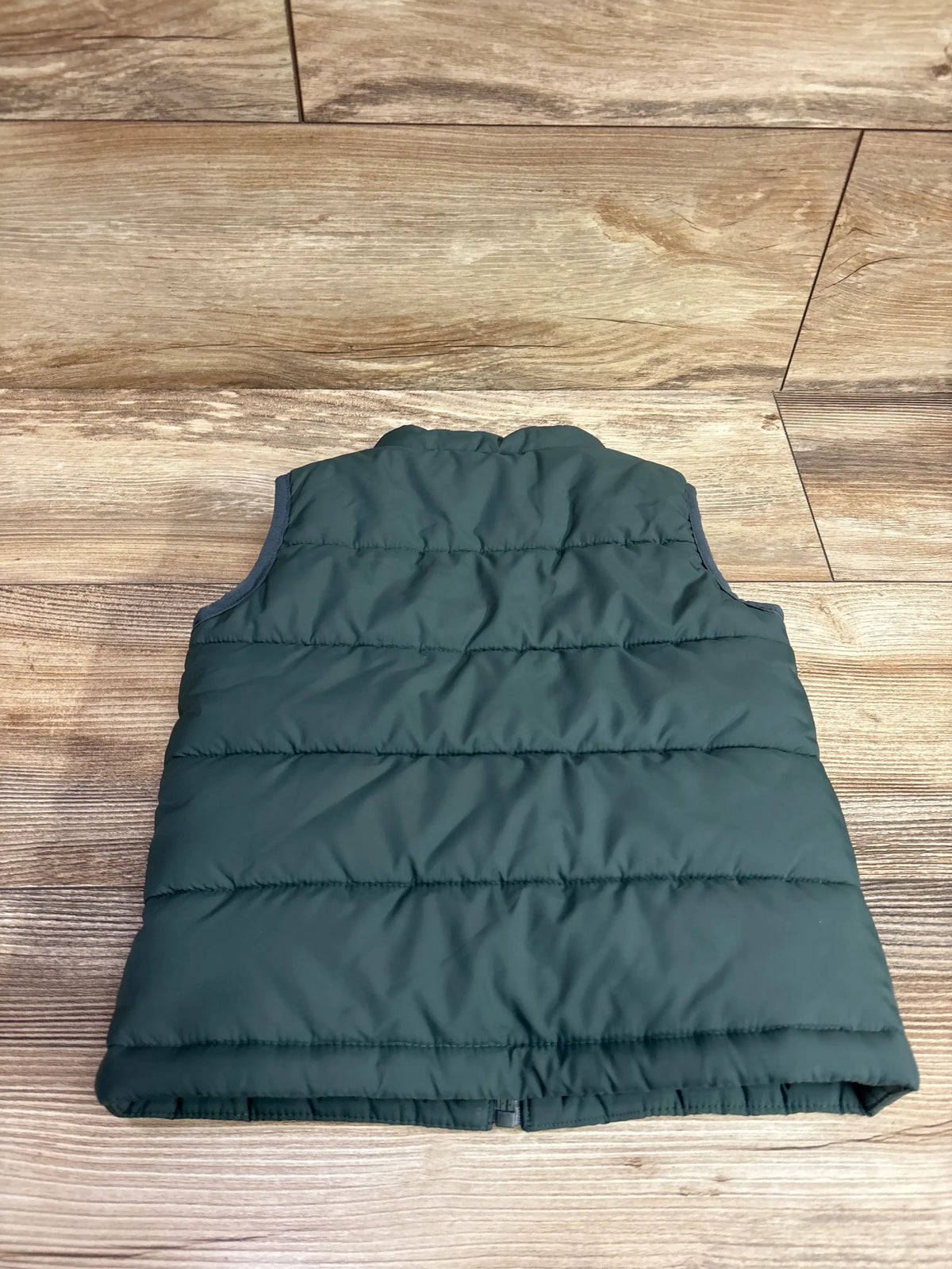 Back view of Nike green puffer vest showcasing horizontal quilted panels with a wood floor background