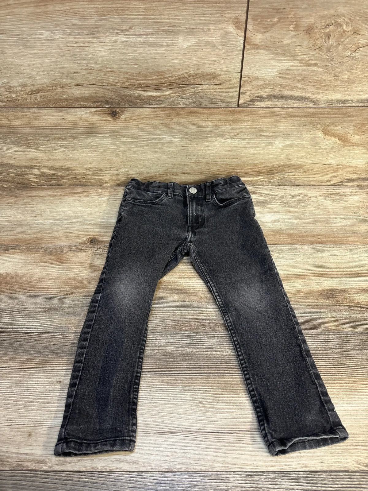 Black denim kids jeans laid flat on wood background, children's clothing resale