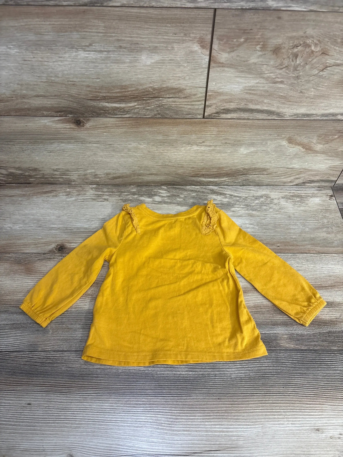 Yellow long-sleeve baby shirt with lace ruffle details on wooden floor