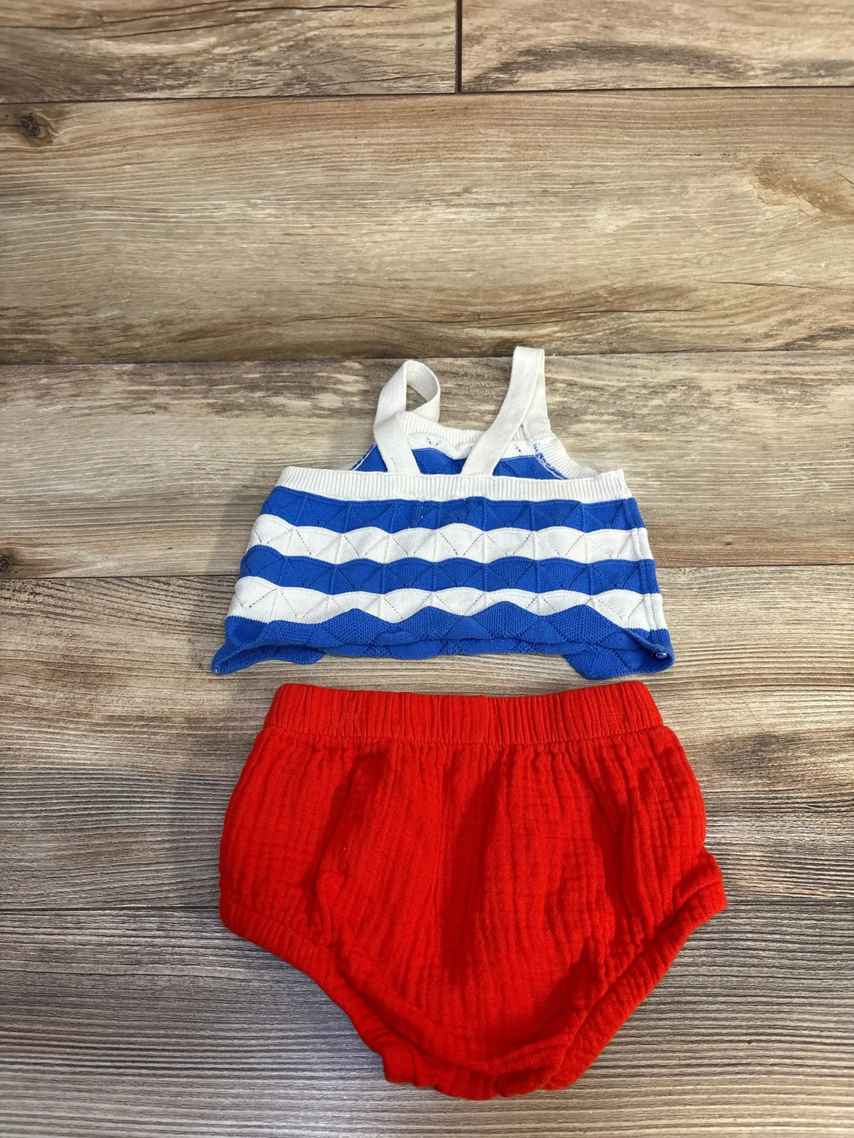 Flat lay of Cat and Jack 2-piece 4th of July set with blue-white tank, white straps, and red bloomers on wood background