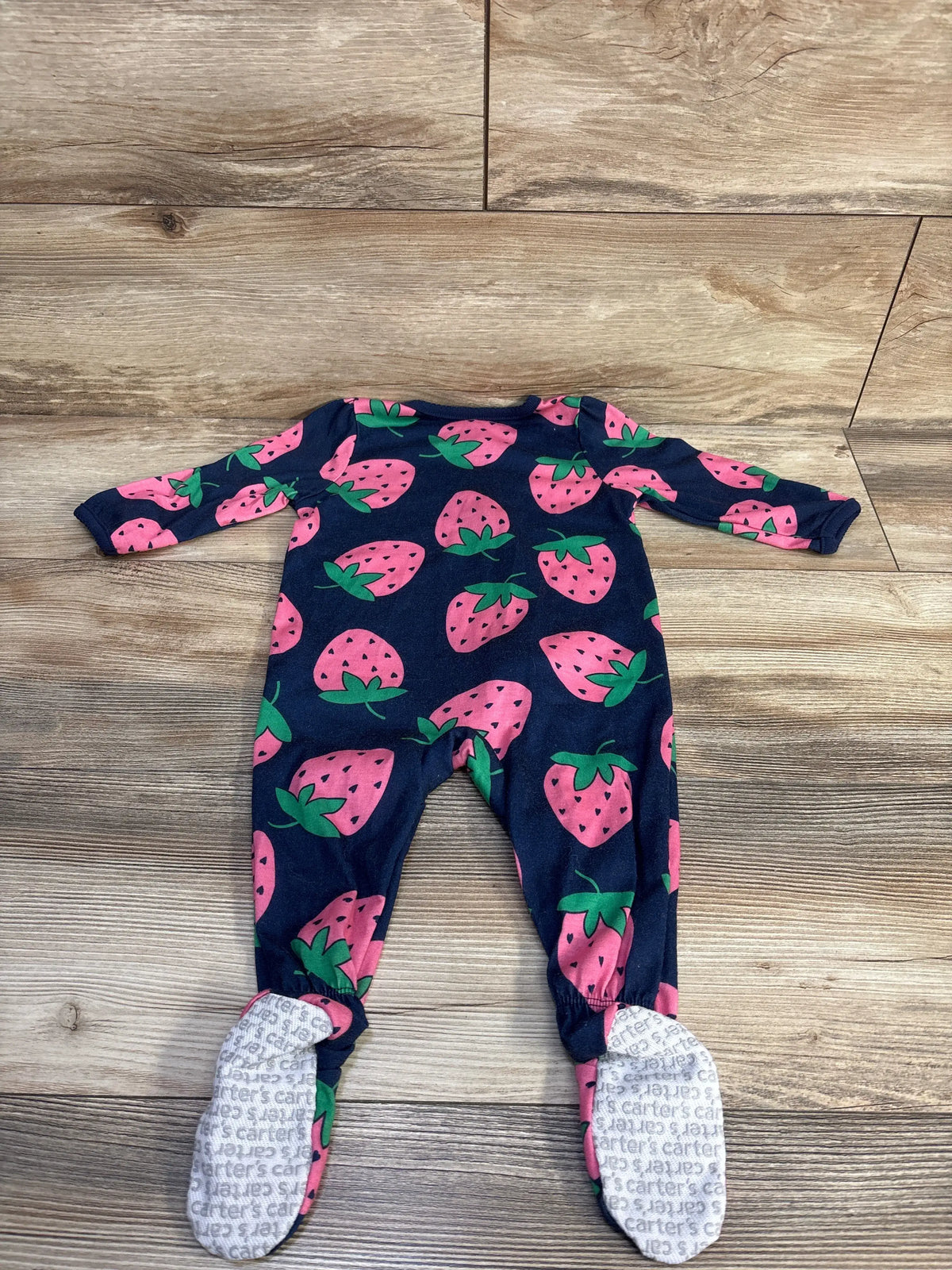 Front view of Simple Joys strawberry print sleeper in navy showcasing footed legs on a wood-look background