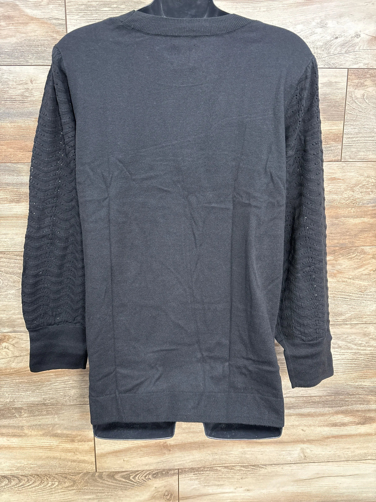 Black long-sleeve sweater with textured knit sleeves on wooden floor background