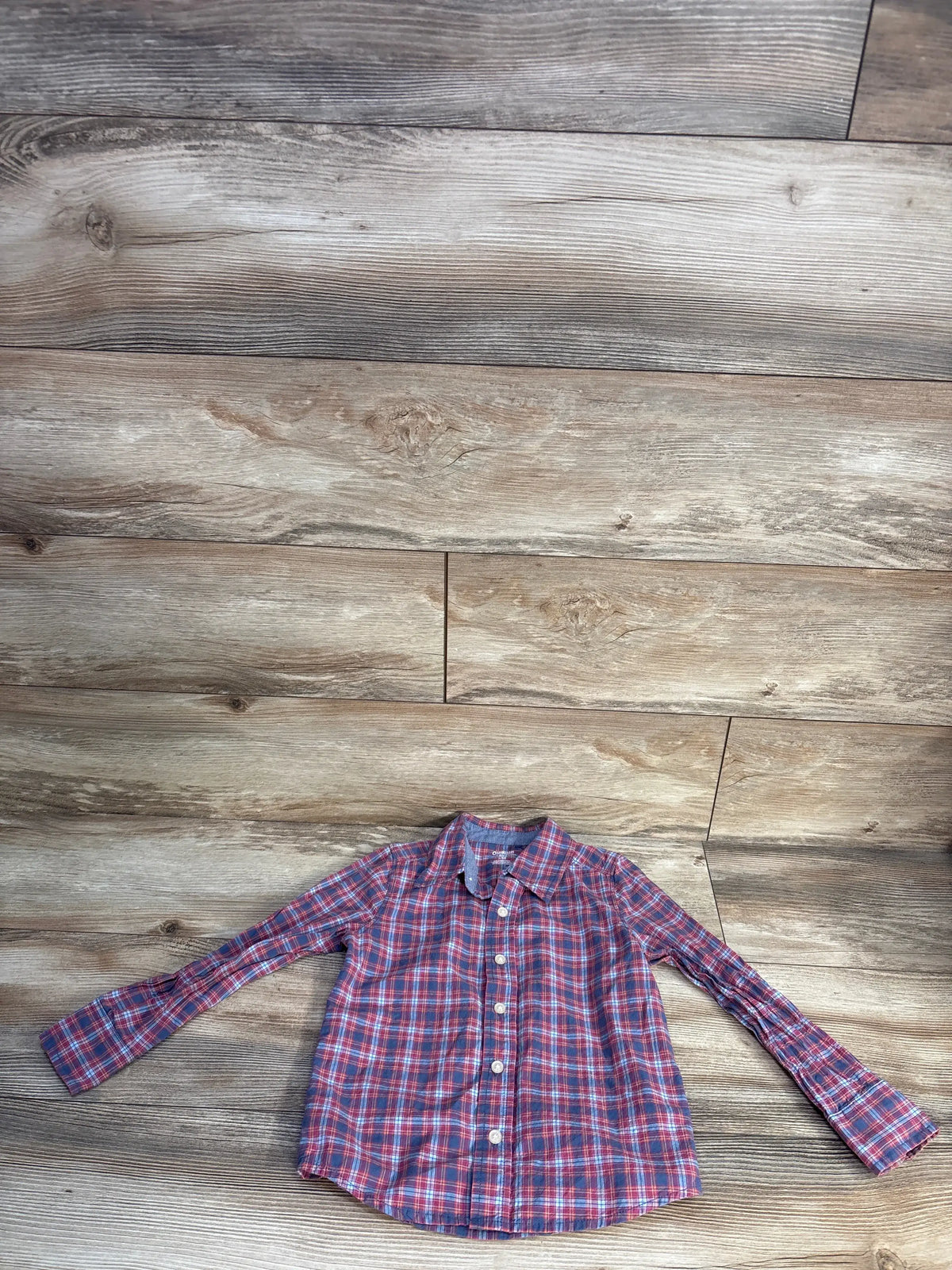 Front view of OshKosh red plaid button-up shirt in size 5T showcasing collared long sleeves on a wood floor