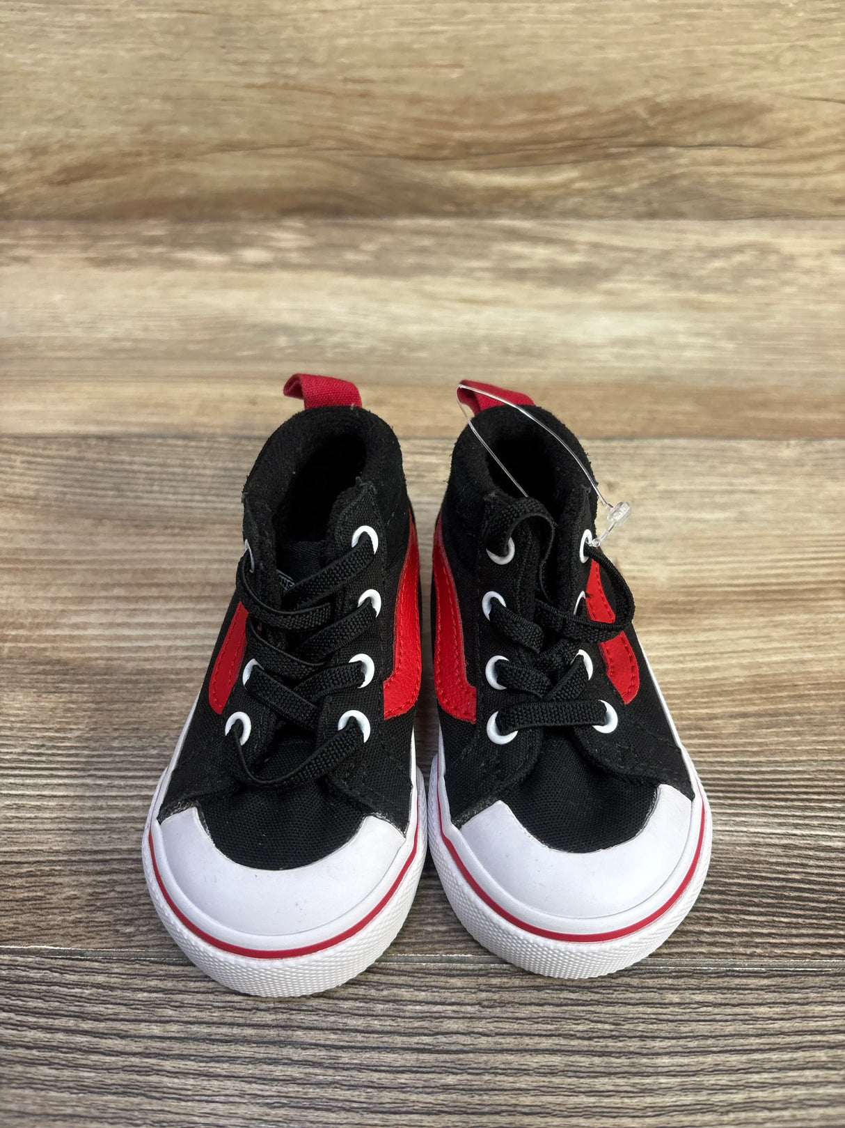 Front view of Vans Racer Mid sneakers showing black canvas with red side stripe and white rubber toe caps on wood background