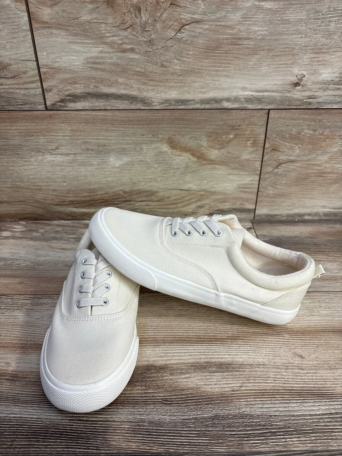 Pair of white canvas sneakers with rubber soles displayed on wooden floor, children's casual shoes