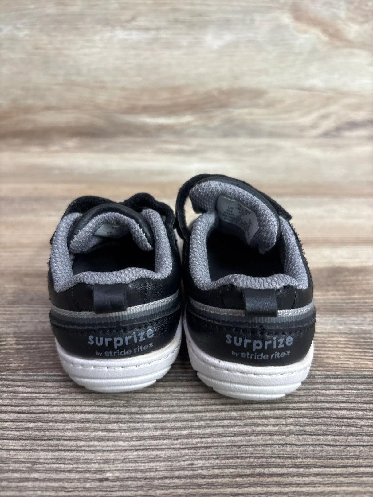 Rear view of Surprize by Stride Rite Killian toddler sneakers showcasing branded heels and white soles on a wood surface