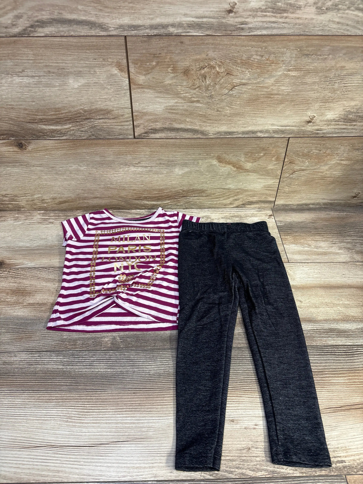 Top-down view of Dream Star 2pc striped shirt and pants set with a sequin graphic shirt and black pants on wood flooring