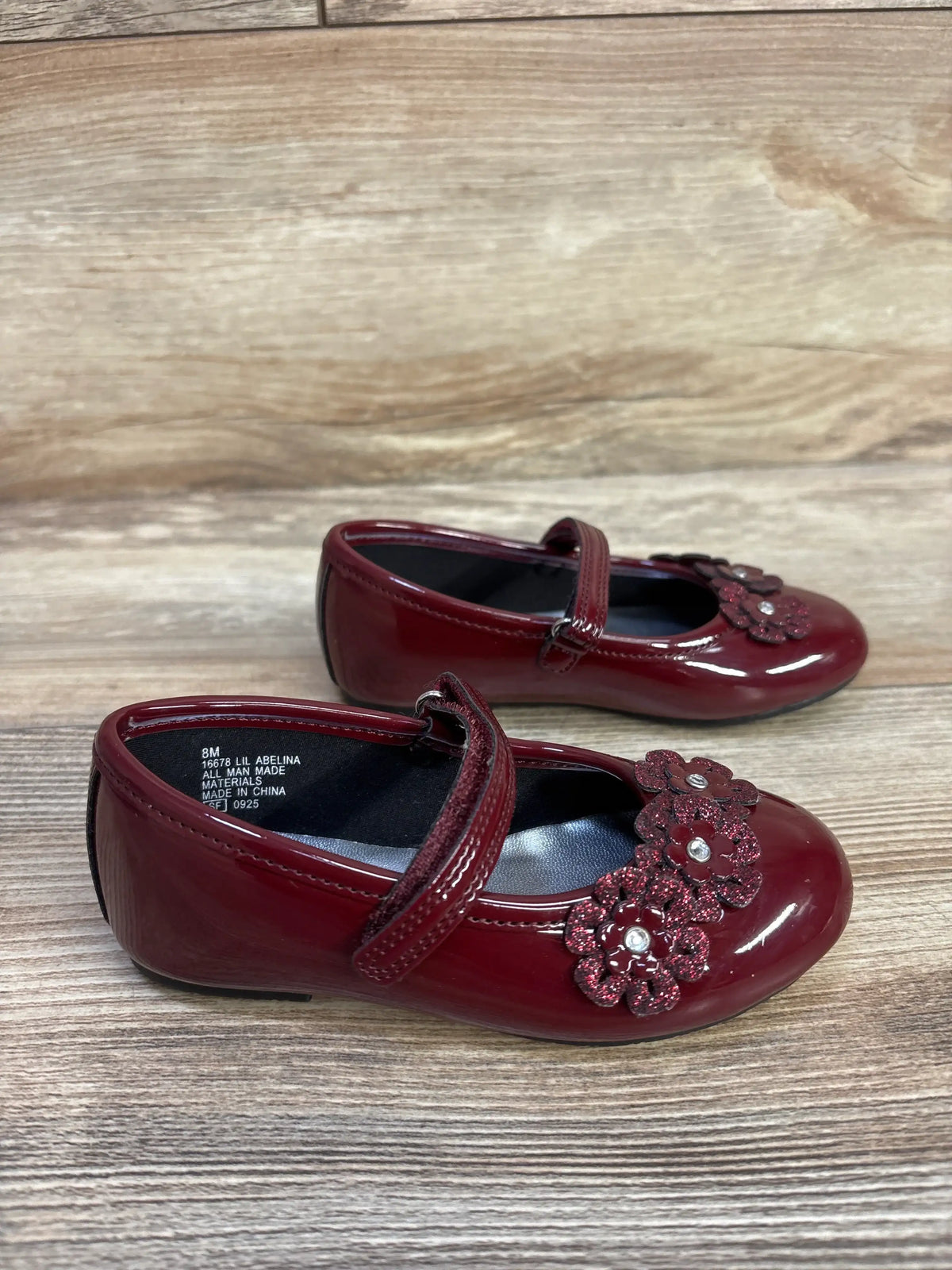Front and side views of Rachel Shoes Lil Abelina flats with burgundy patent uppers, floral vamp accents, and halo straps on wood