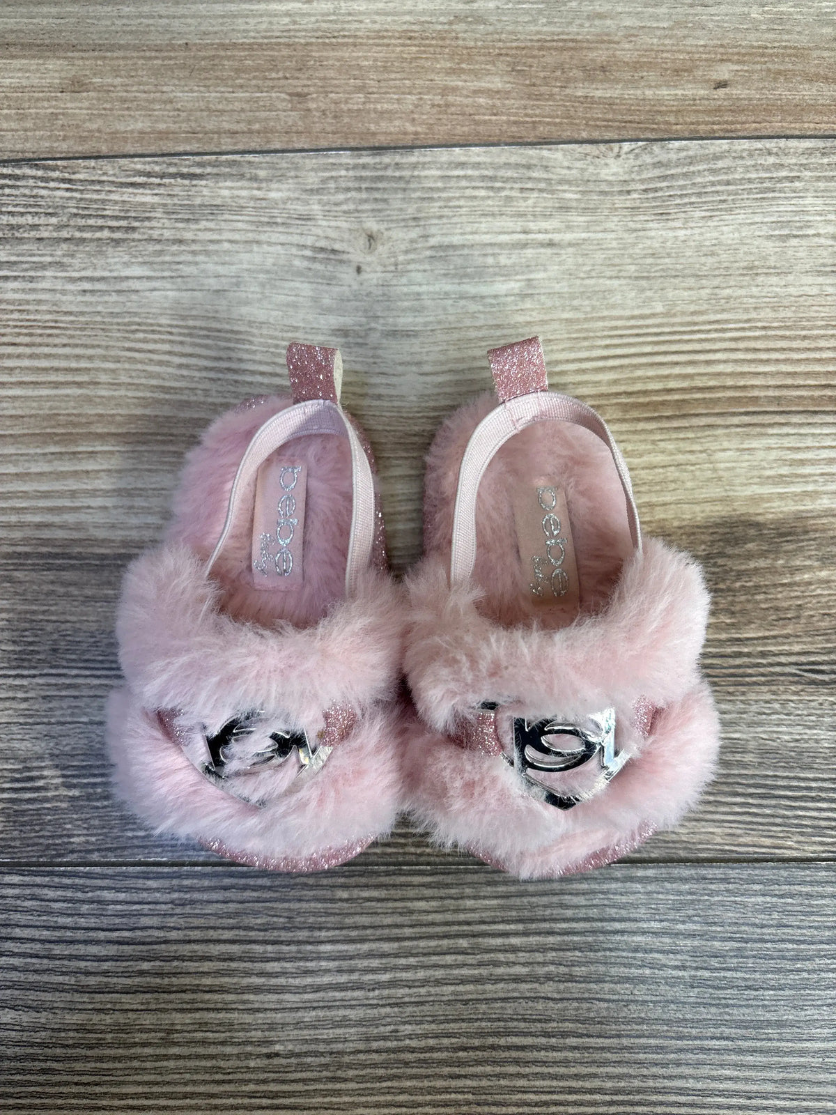 Bebe Babe faux fur slide sandals in pink with silver accents on a wooden background