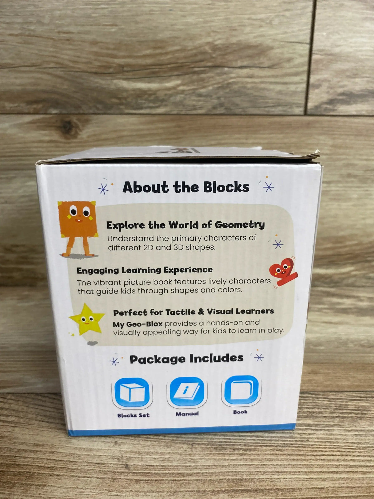 Back view of My Geo-Blox toy box showcasing the 'About the Blocks' text describing learning 2D and 3D shapes and package icons for blocks, manual, book on wood background
