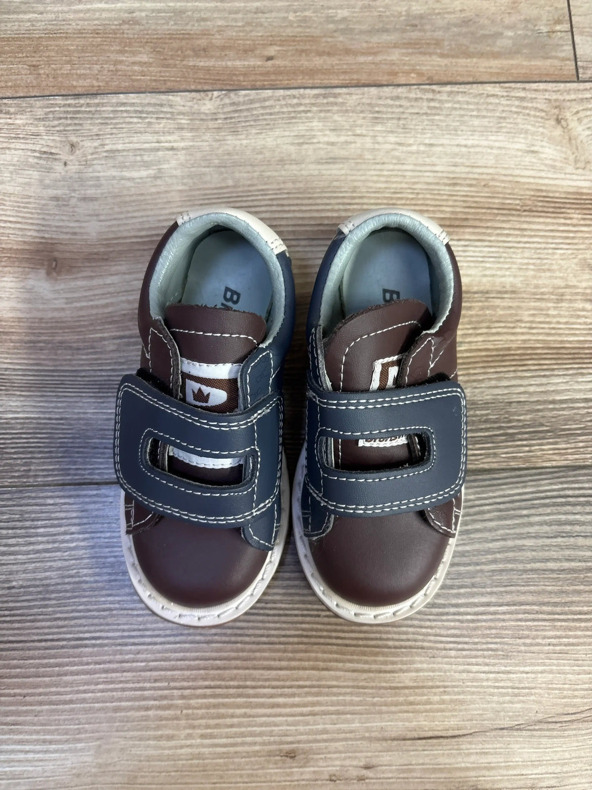 Top view of Brunswick bowling shoes in brown showcasing hook and loop closures with a wood-look floor background