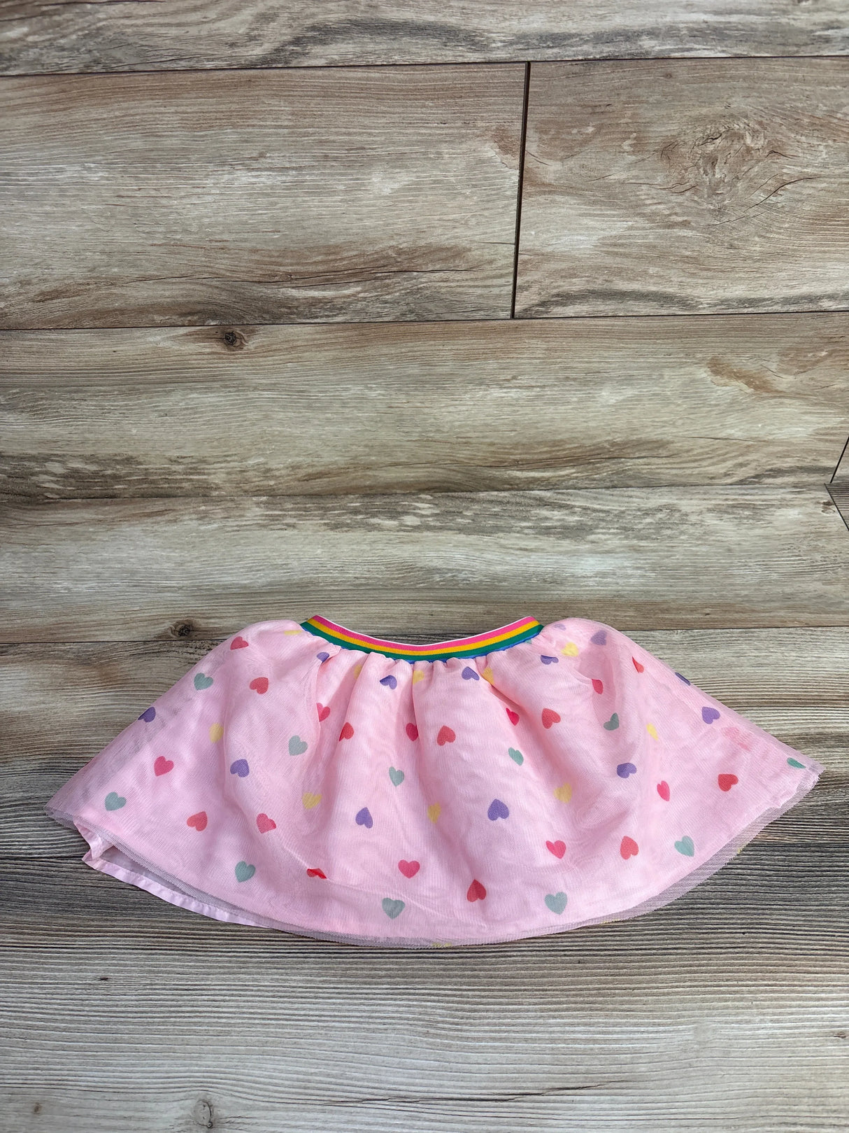 Pink toddler skirt with multicolored heart print and rainbow elastic waistband on wood floor